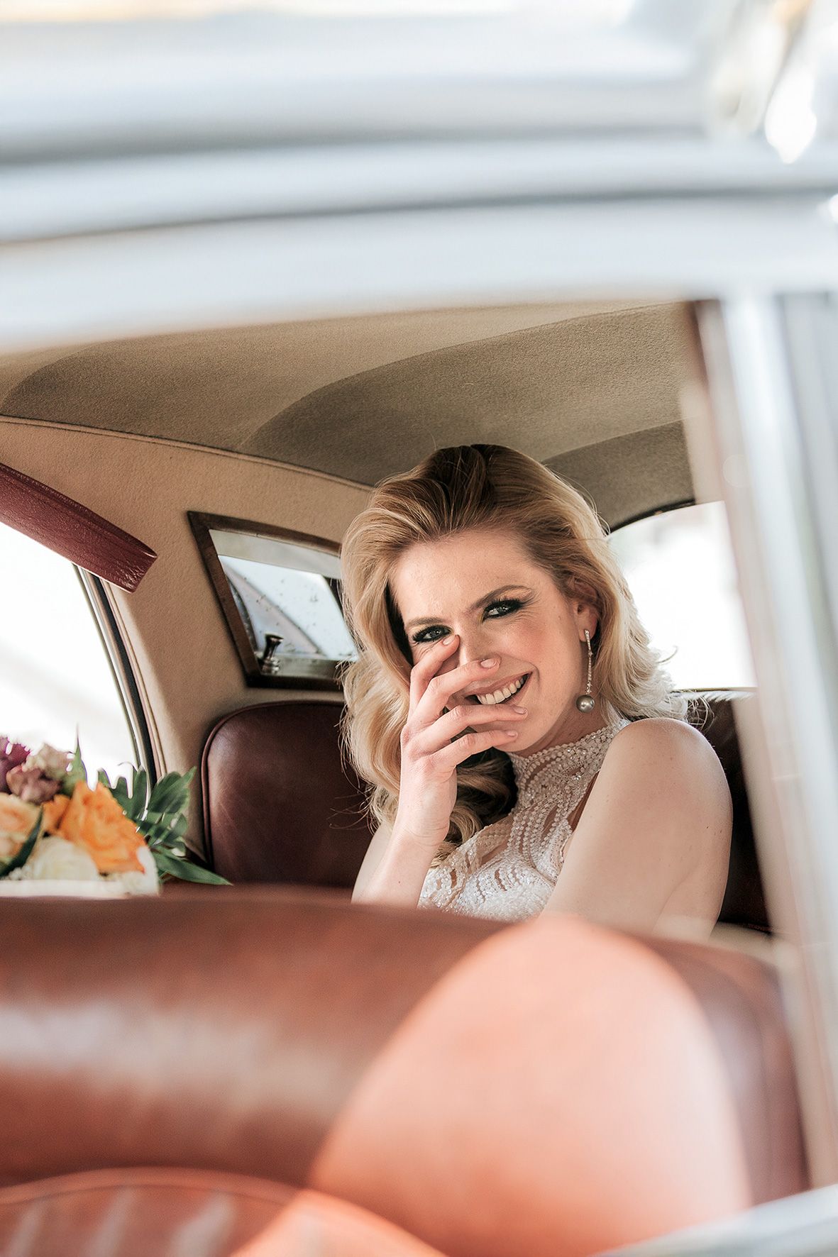 View through car window showing luxurious tan leather interior with floral arrangement visible.