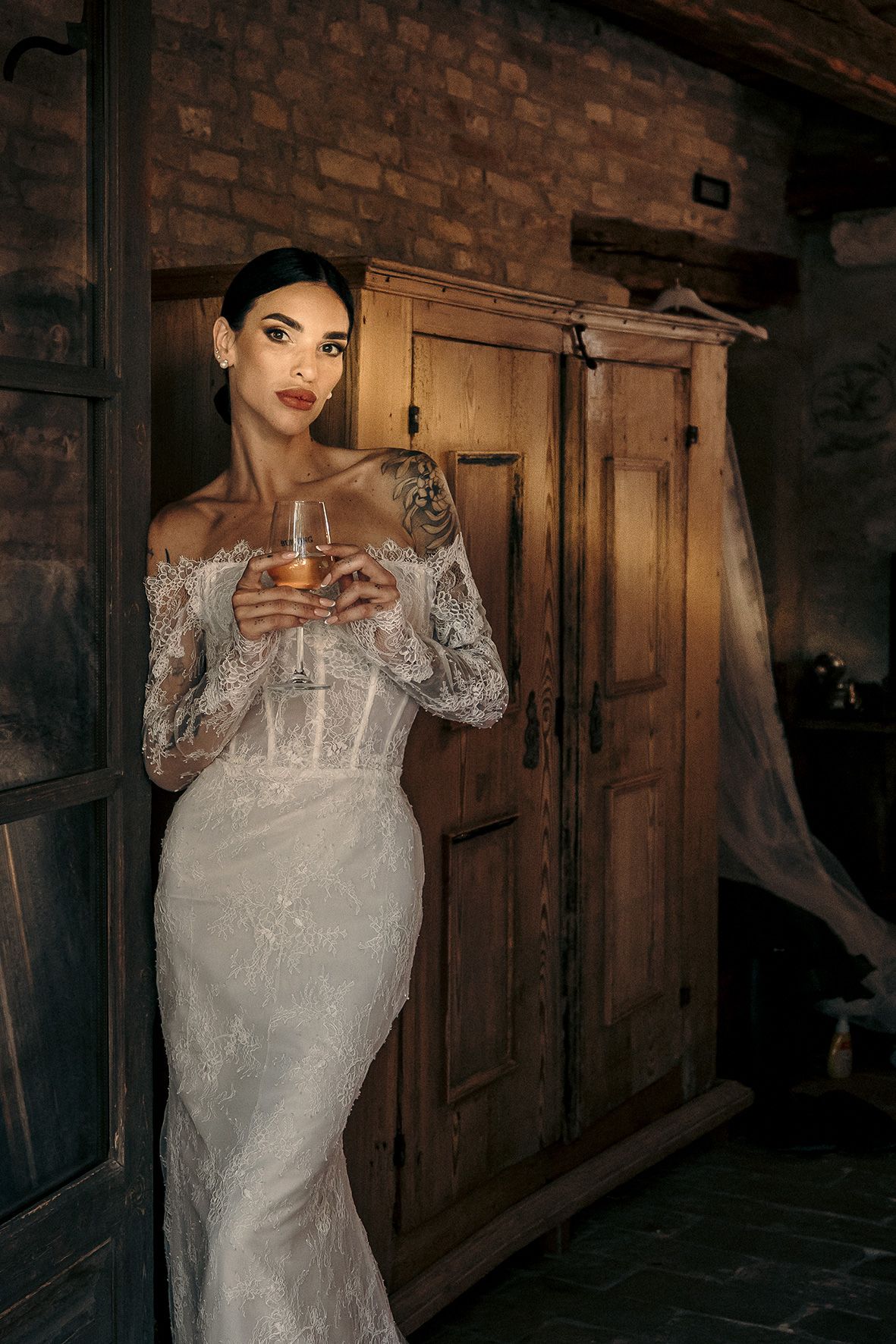 Elegant off-shoulder lace wedding dress with corset detail photographed in rustic setting with wooden wardrobe.