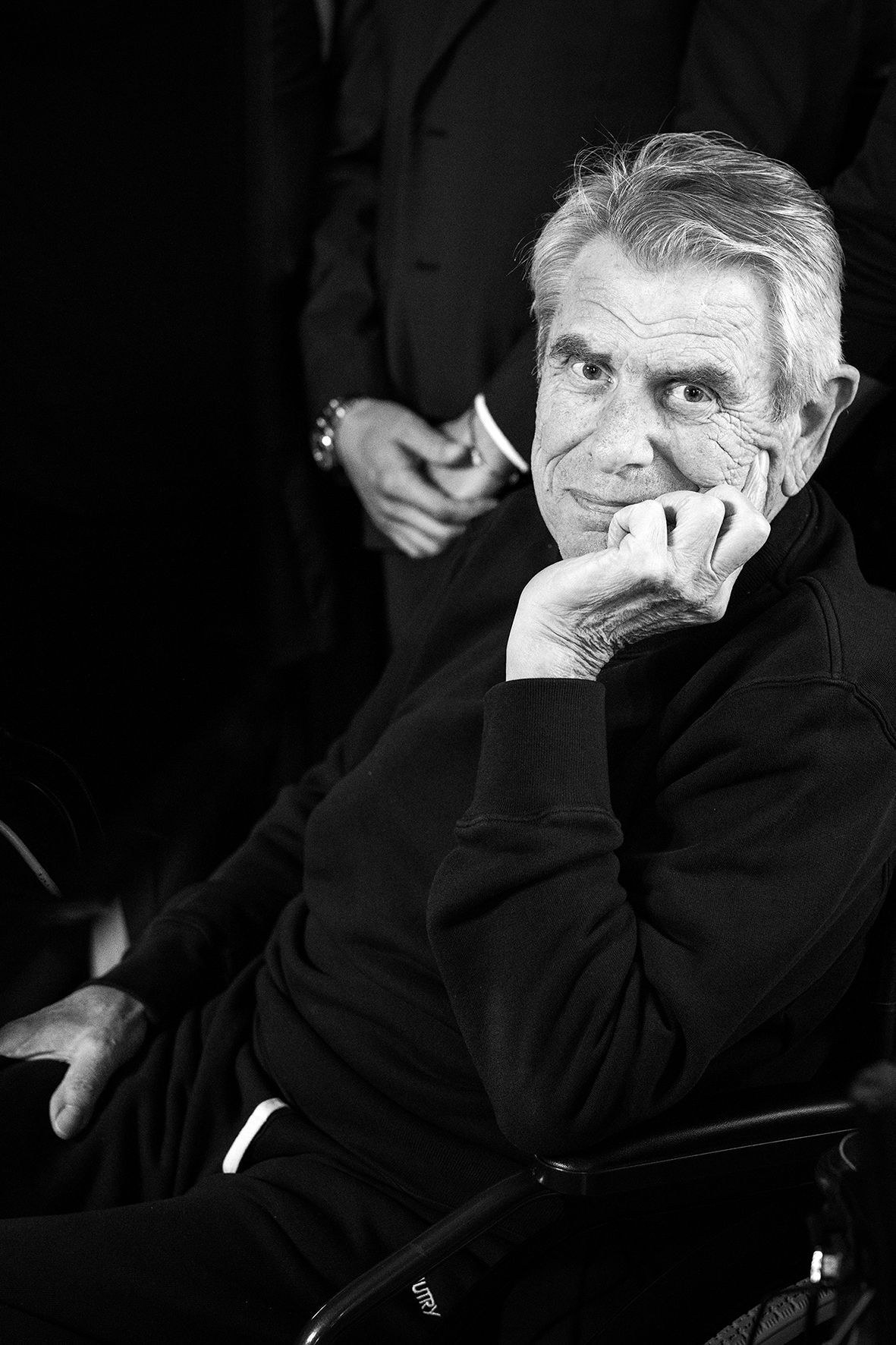 A black and white portrait of an older gentleman in dark attire resting his chin on his hand in contemplation.