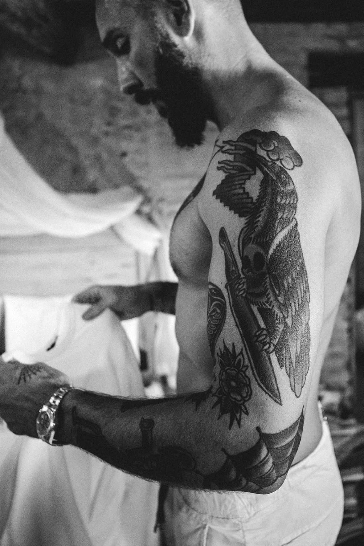 Black and white photo shows a person displaying a large eagle and floral tattoo on their upper arm and shoulder area.