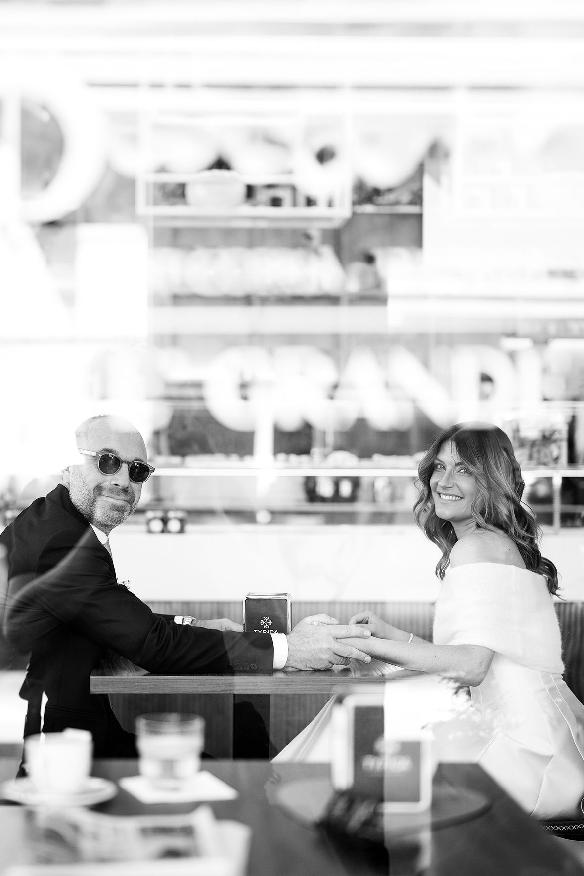 A black and white photo of two people sitting at a cafe table, sharing a casual moment together.
