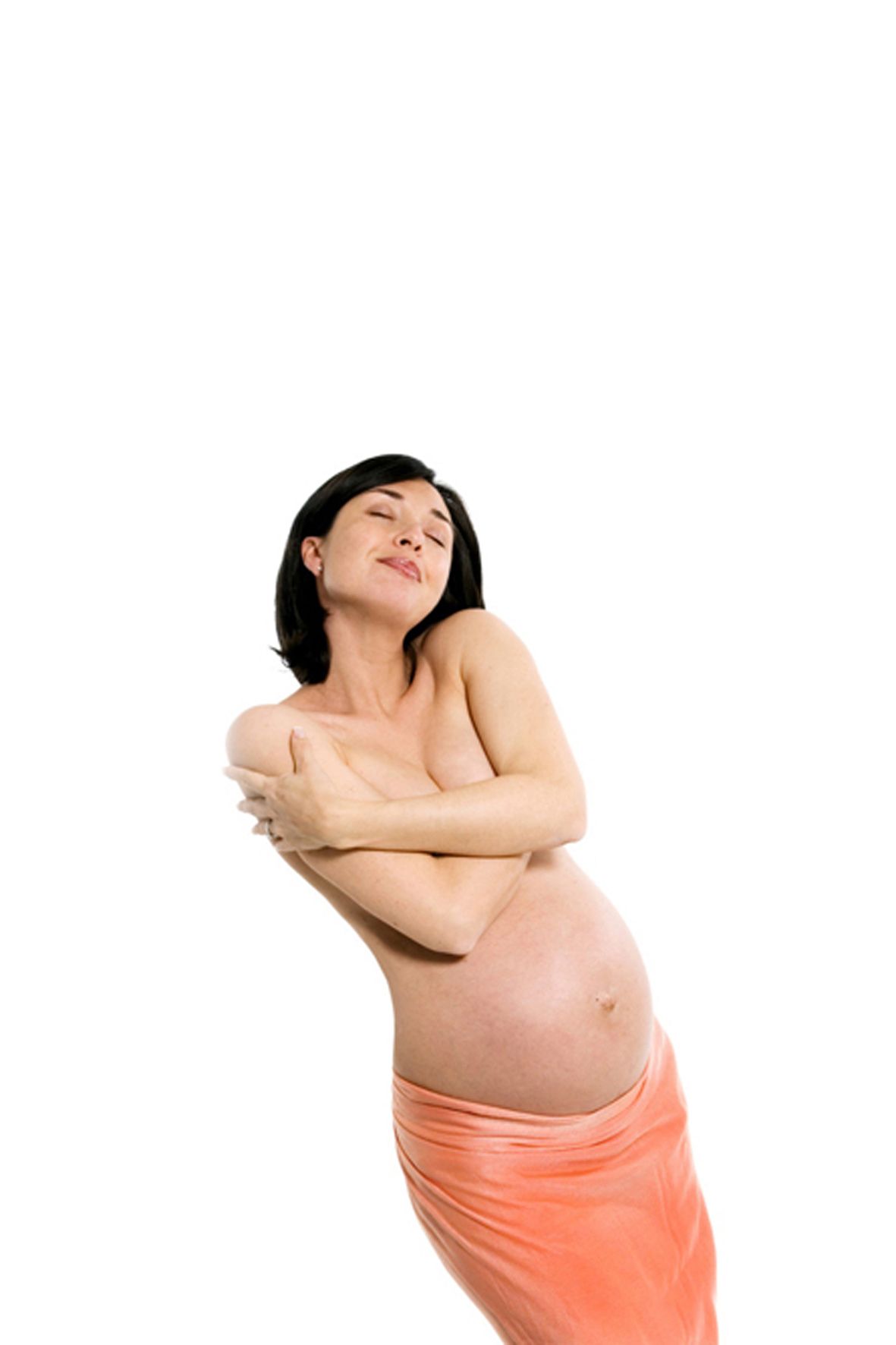 A pregnant woman wearing a peach-colored skirt poses topless against a white background.