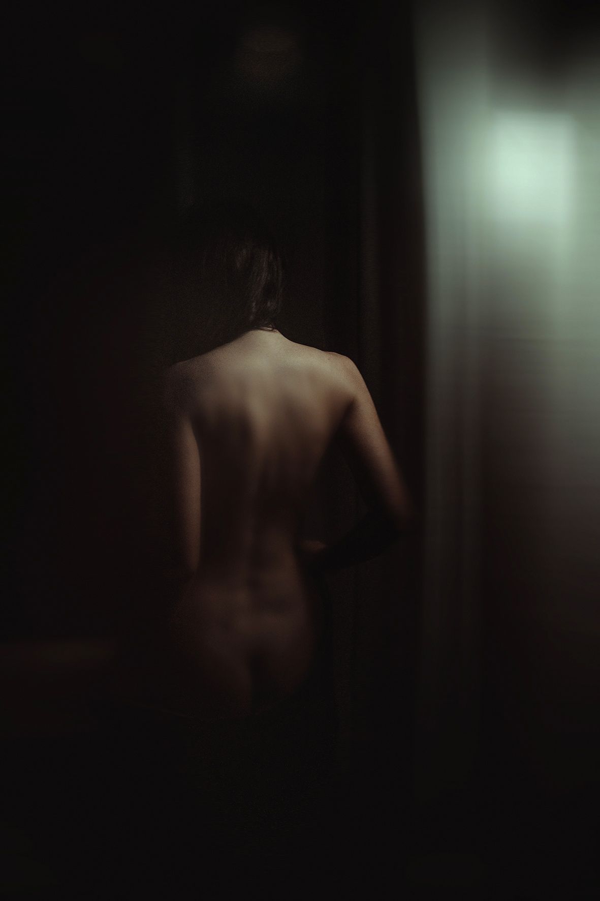 A moody and artistic silhouette photograph showing a bare back figure in dark atmospheric lighting.