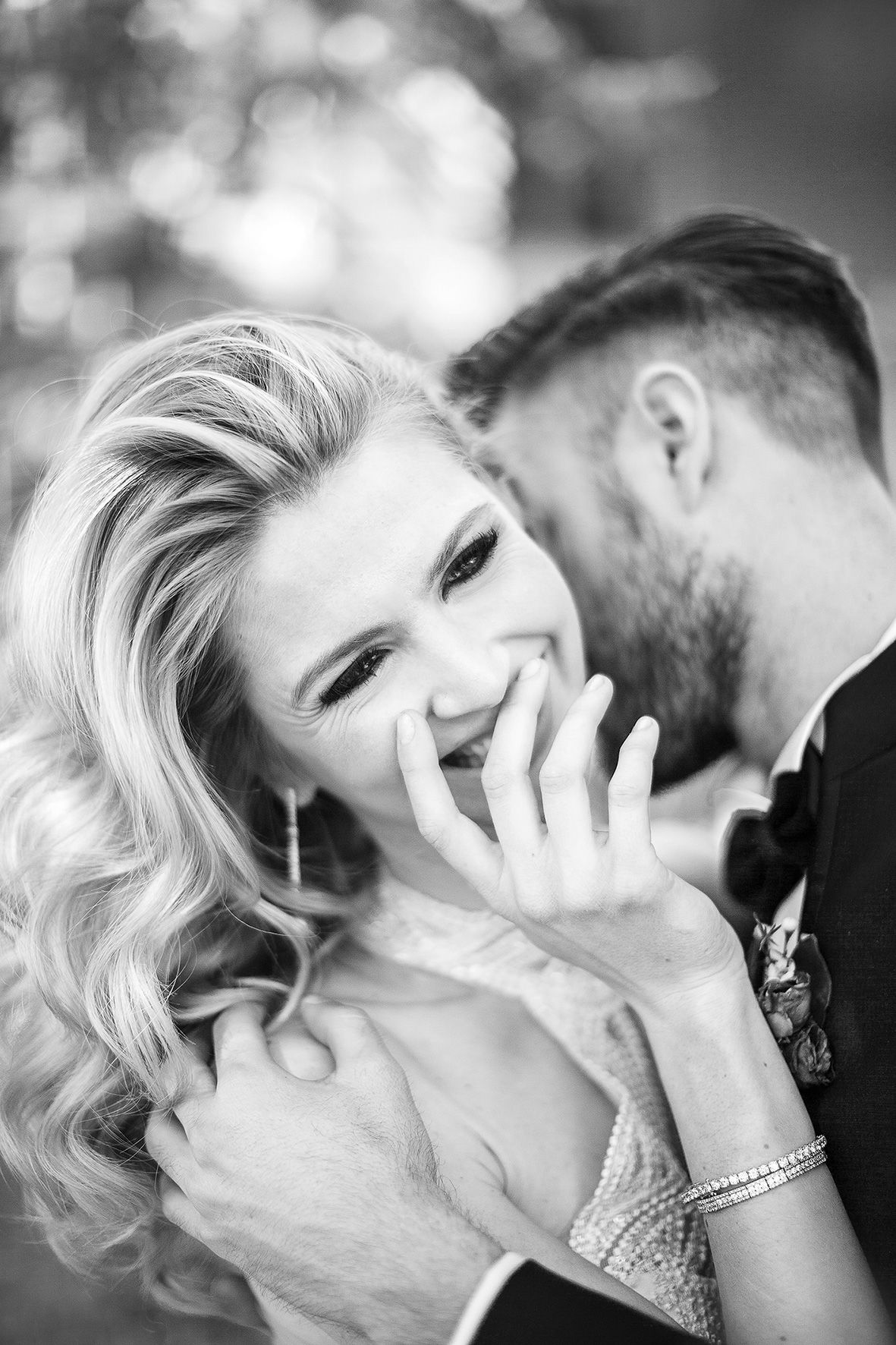 A candid black and white wedding photo of a laughing bride wearing a sparkling dress while sharing an intimate moment.