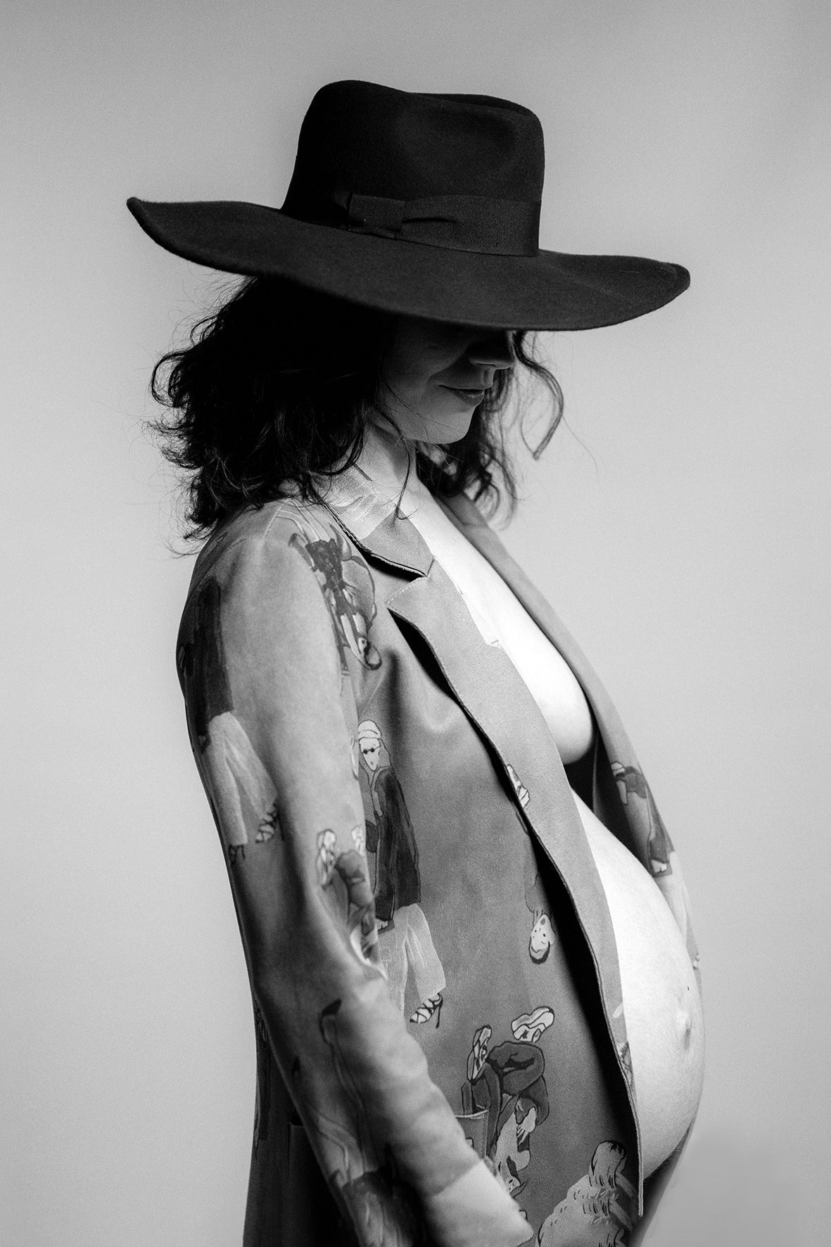 Black and white portrait of a person in a wide-brimmed hat and patterned jacket looking down in profile.