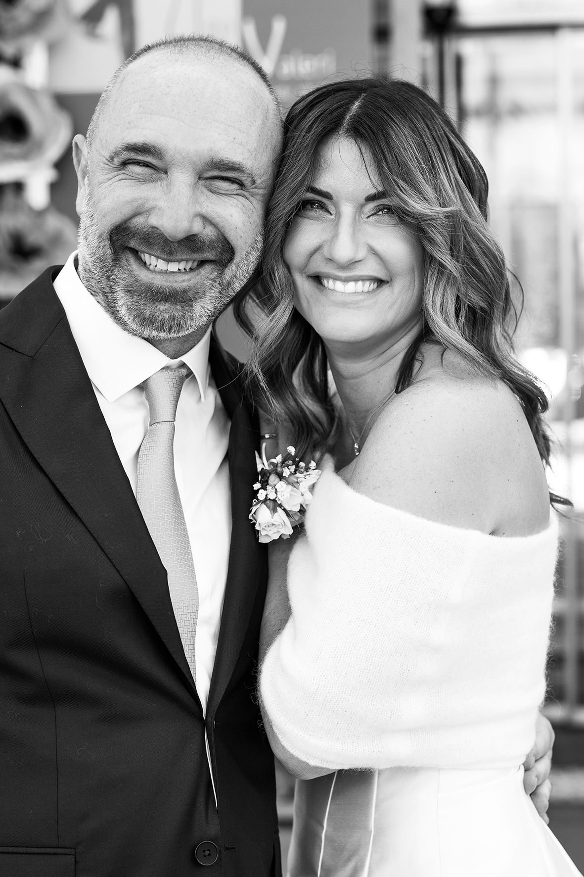 Black and white wedding portrait showing a couple smiling together, with the bride in an off-shoulder dress and groom in suit.