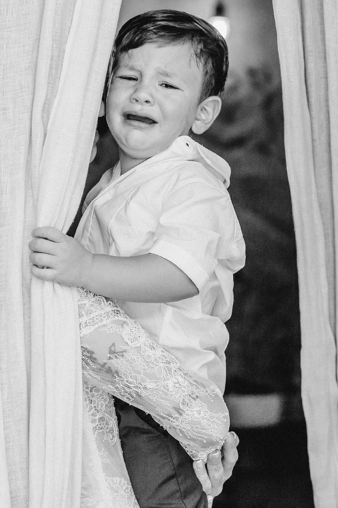 A young child in a white shirt laughs while playing with curtains in this black and white photograph.