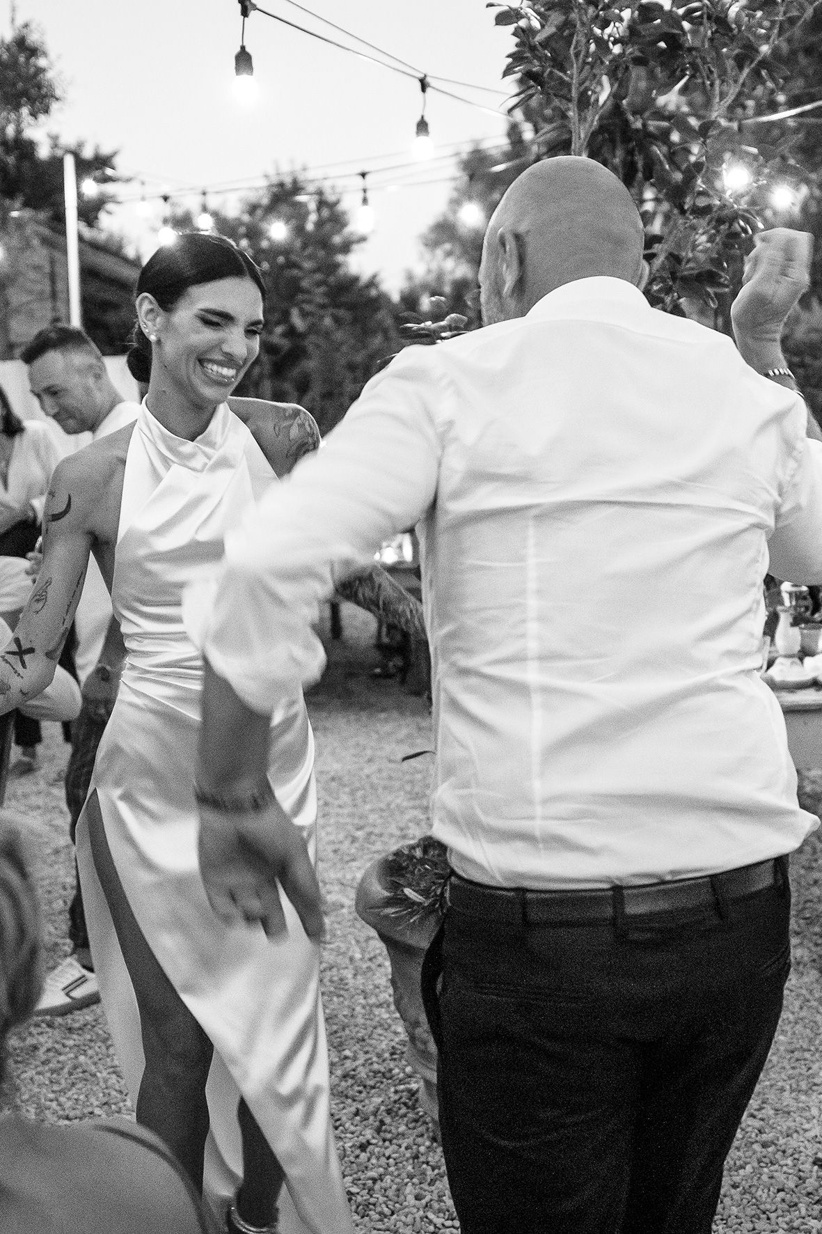 A couple dances together at an outdoor wedding reception with string lights hanging overhead in black and white.