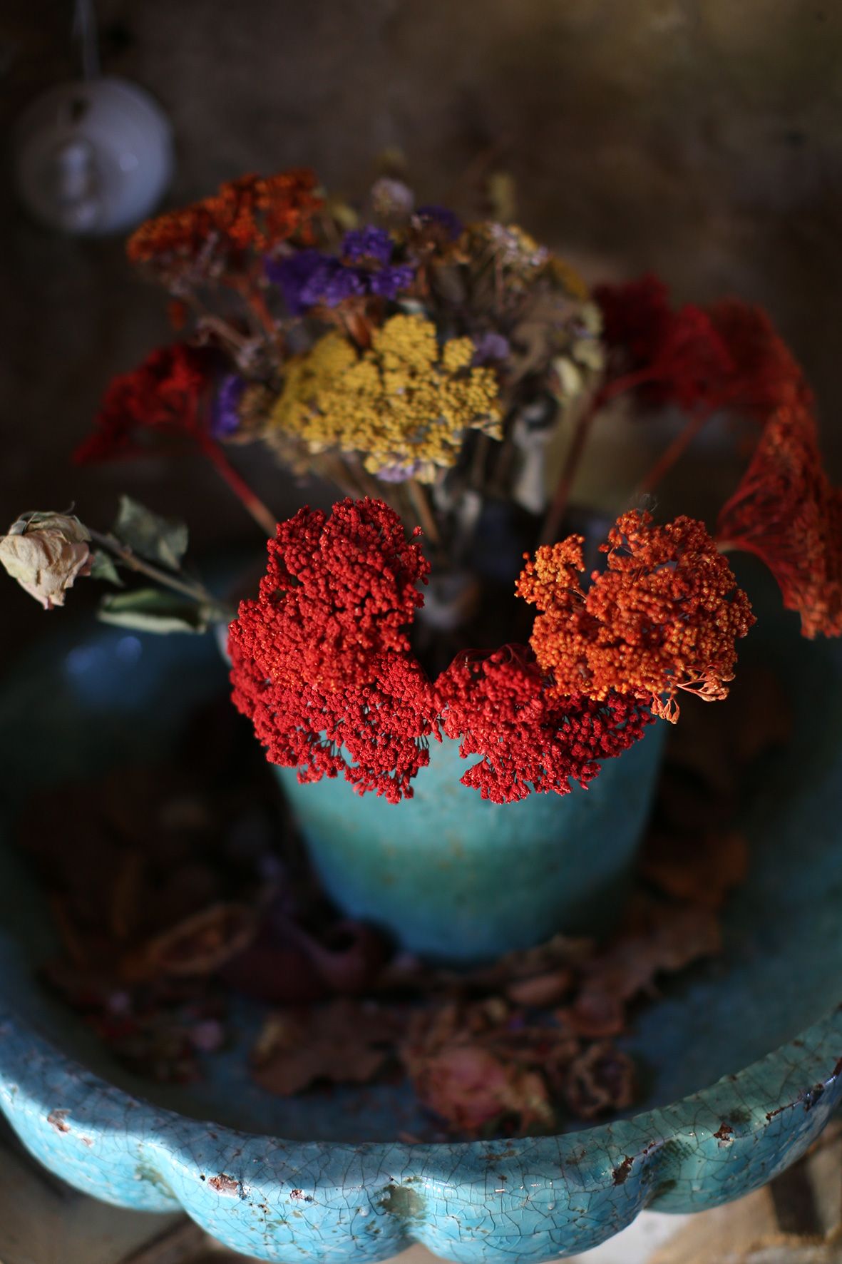 A vintage turquoise vase holds dried red, yellow and purple flowers arranged in a rustic autumn display.