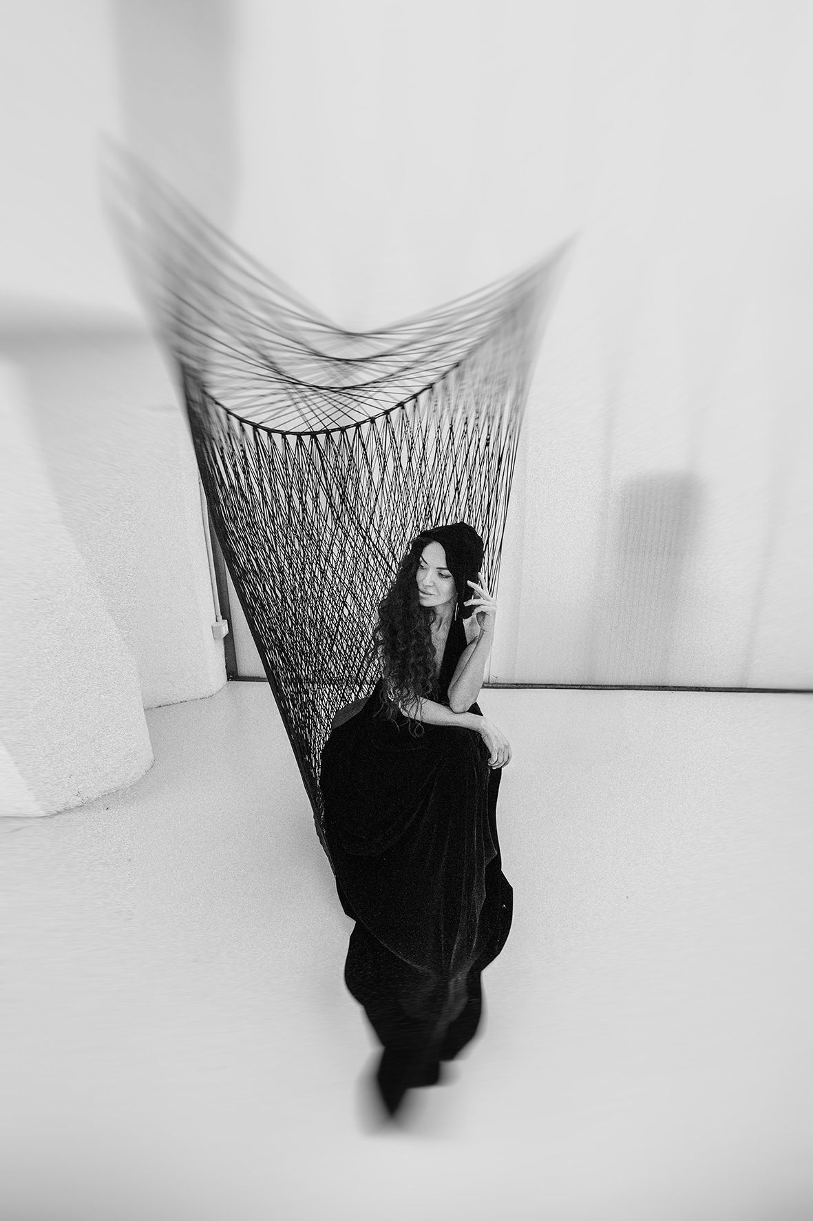 Black and white artistic photograph showing figure in dark clothing against geometric string art installation.