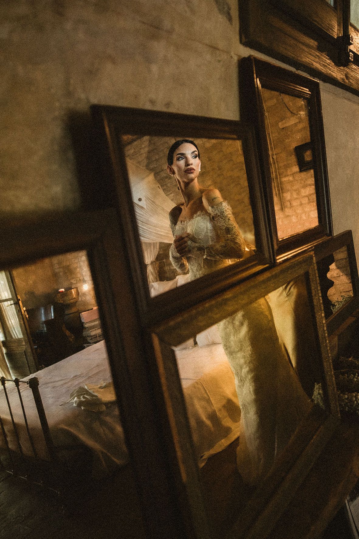A reflection in a divided window pane shows a bride in a white lace gown in warm, moody lighting.