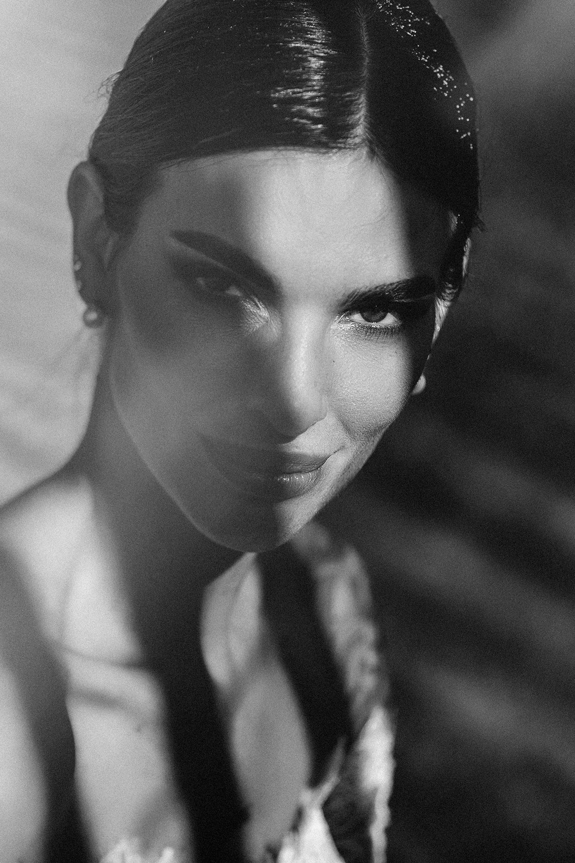Black and white artistic portrait photograph with dramatic lighting and shadows emphasizing elegant features and styling.