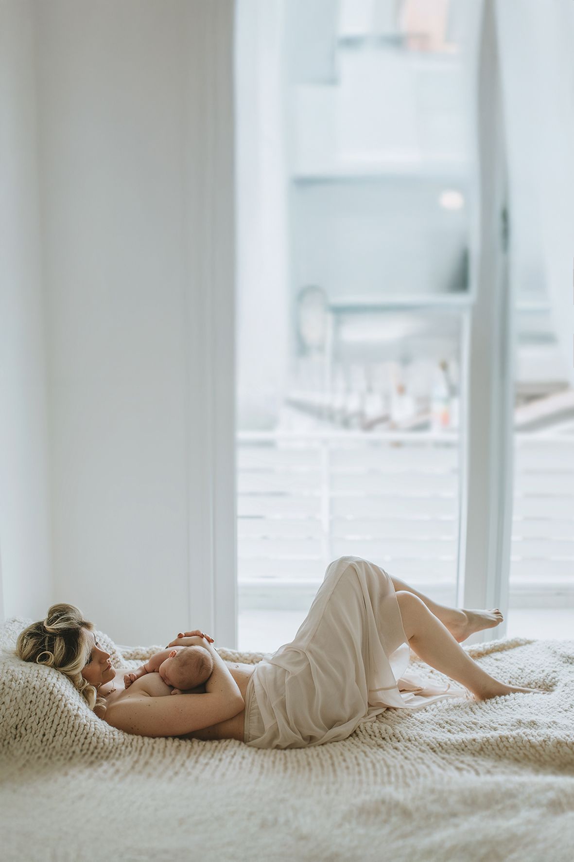 Person relaxes on a plush white carpet by a bright window wearing cream-colored loungewear in a serene setting.
