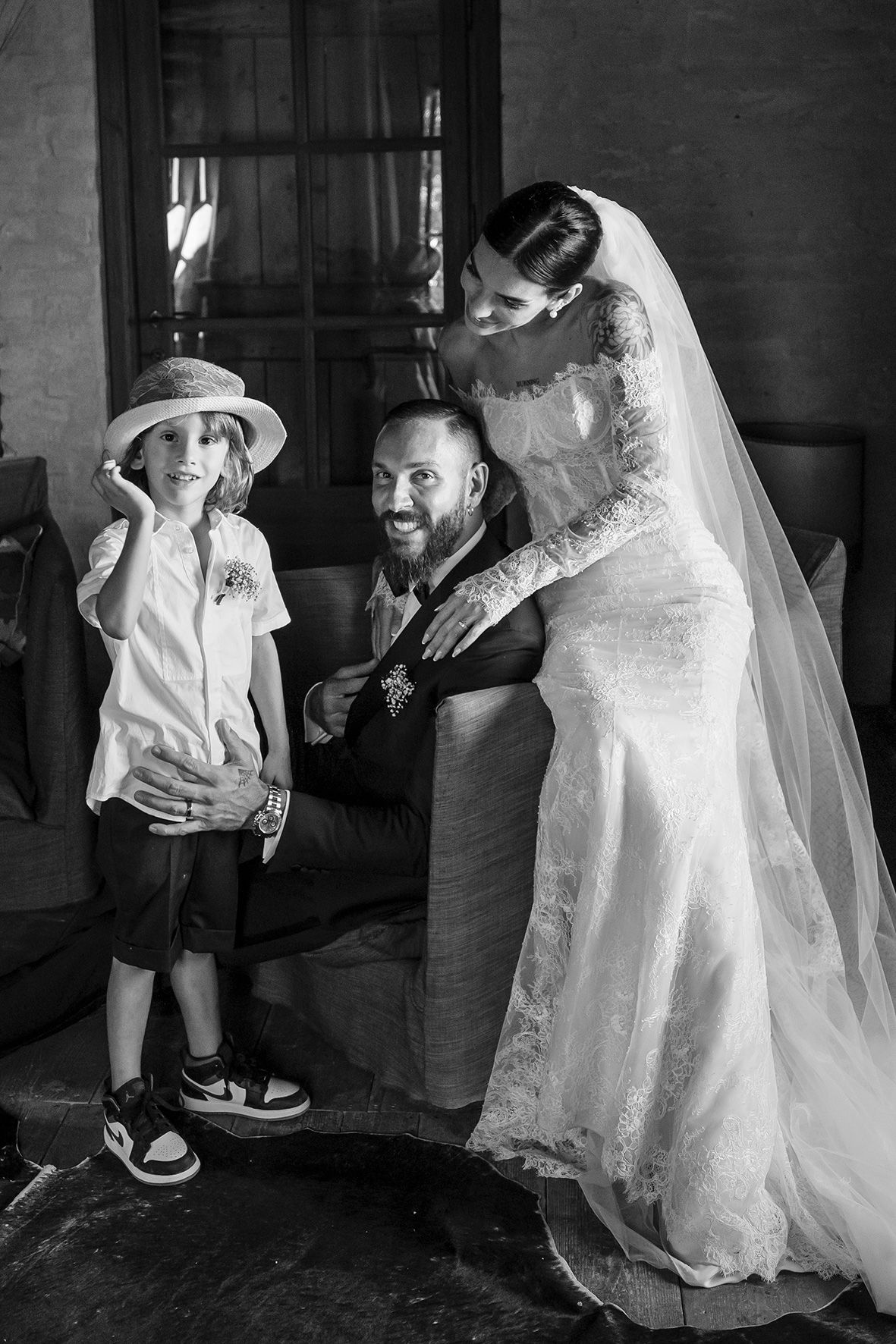 Black and white wedding photograph showing a young child in a hat with a groom and bride in a lace dress and veil sharing a moment.