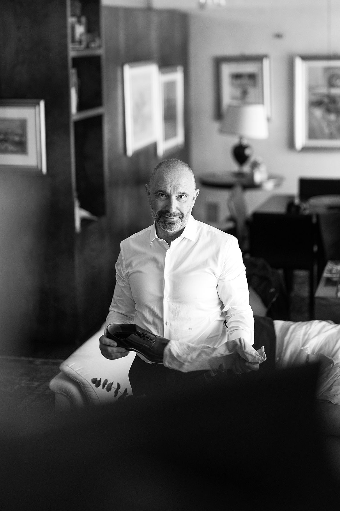Black and white portrait of someone in a white button-down shirt sitting on a couch in a living room with framed art.