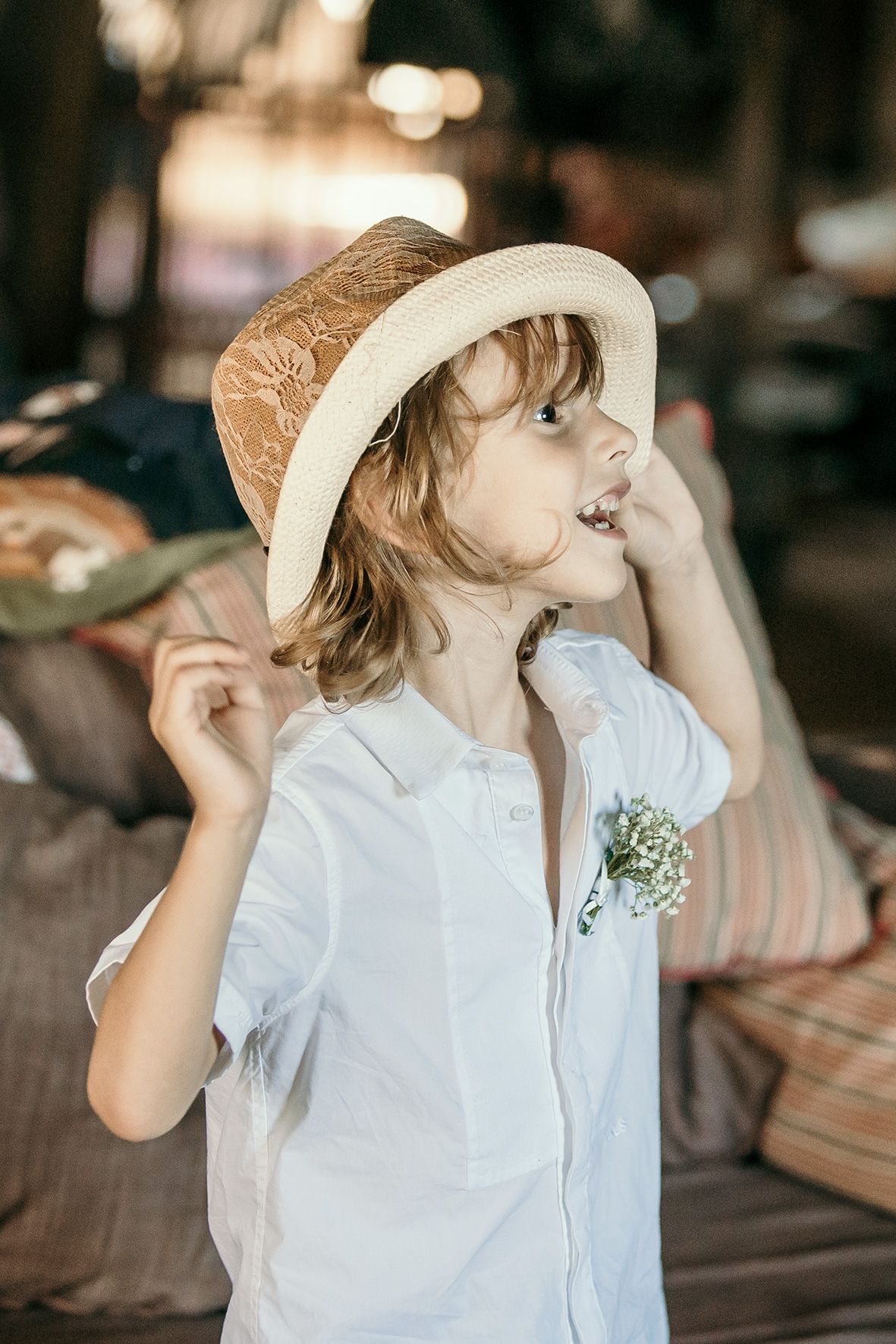 Smiling child in white button-down shirt and straw hat with small boutonniere enjoying an outdoor moment.