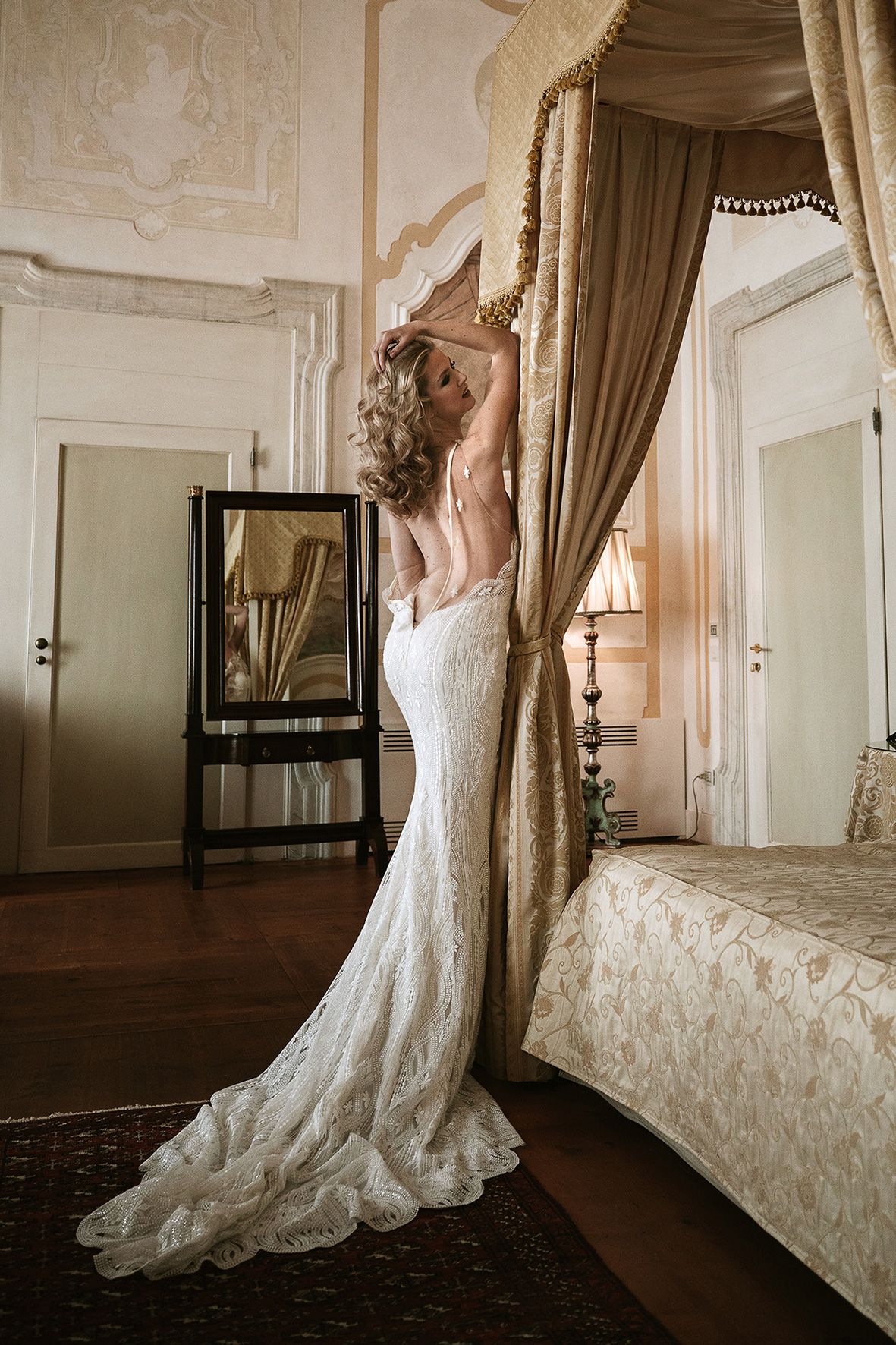 Elegant lace wedding dress with a flowing train elegantly displayed in an ornate vintage-style bedroom interior.