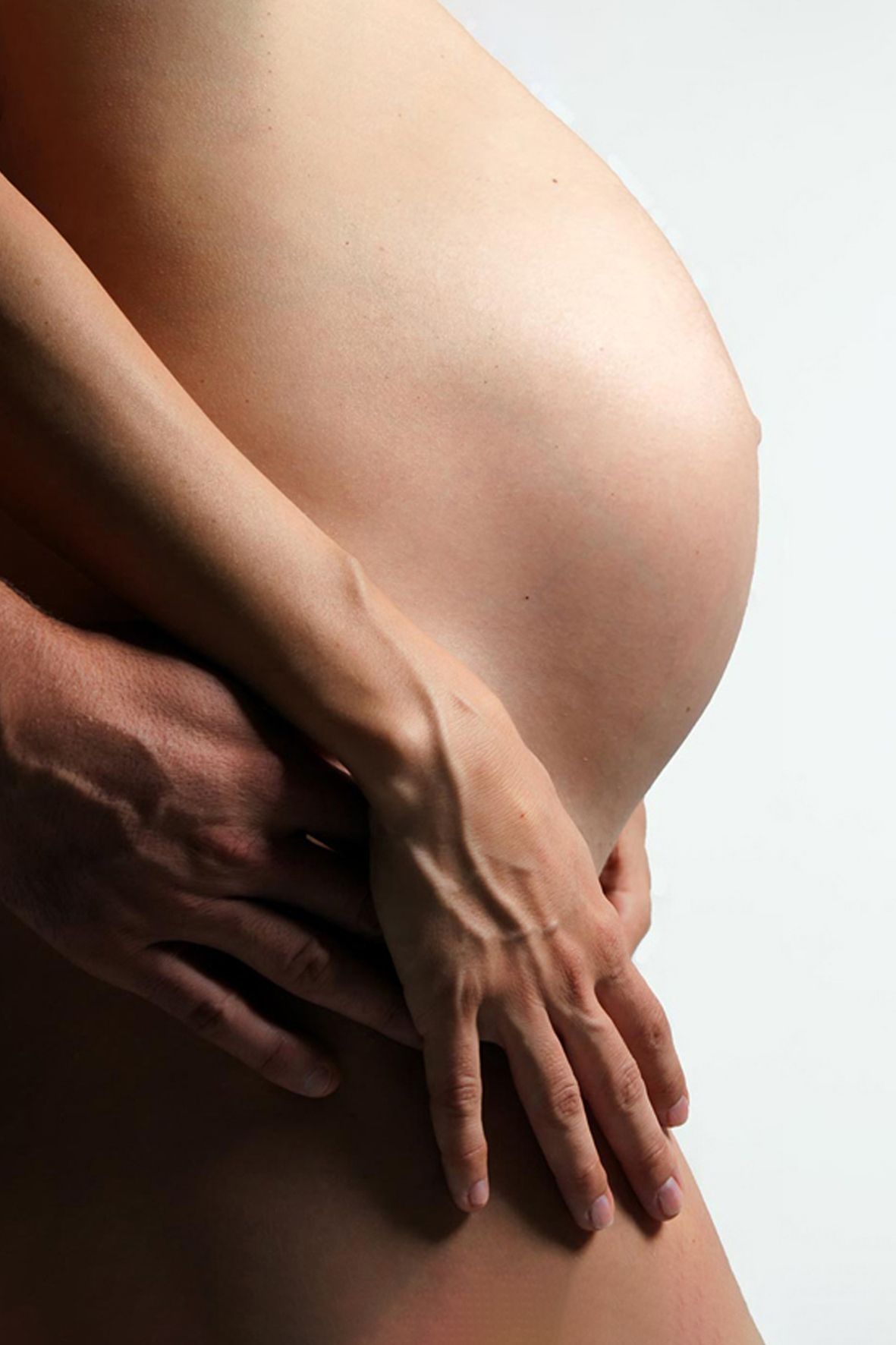 Close up view of a pregnant woman's belly with hands gently resting on the bare skin against white background.
