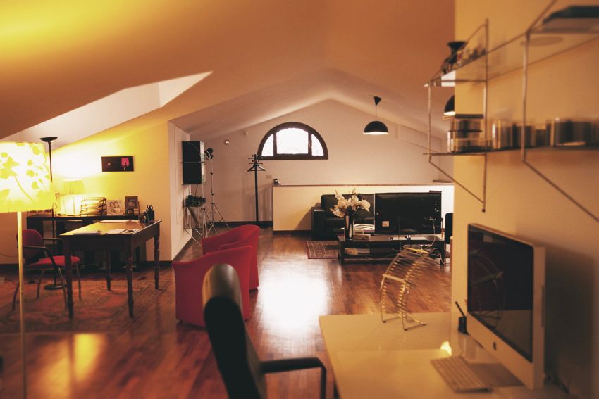 Modern loft apartment interior with wooden floors and arched window under warm lighting.