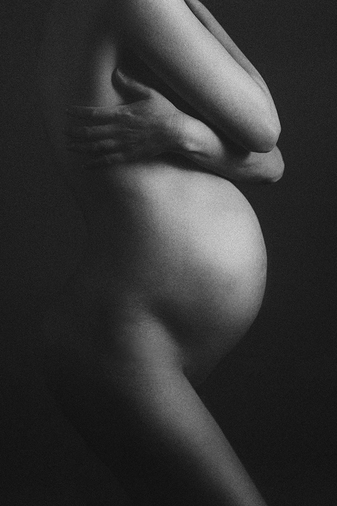 Black and white artistic nude photograph showing the silhouette of a pregnant belly in dramatic side lighting.