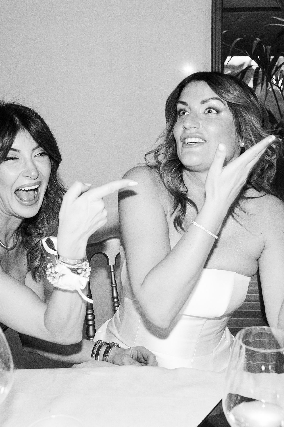 Two women laugh joyfully together at a social gathering in black and white photography.