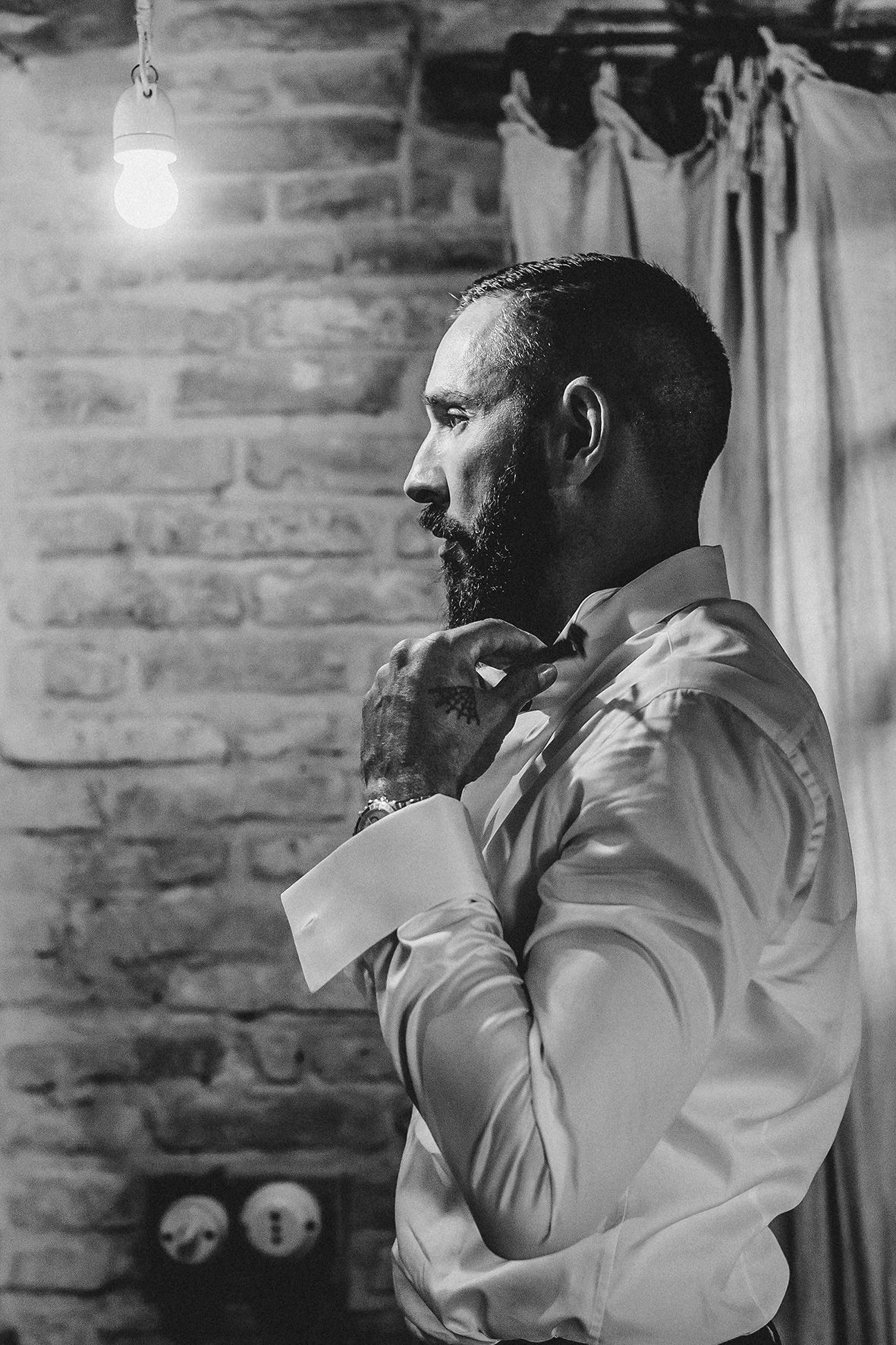 Side profile of someone in a white dress shirt adjusting their collar against a rustic brick wall background.
