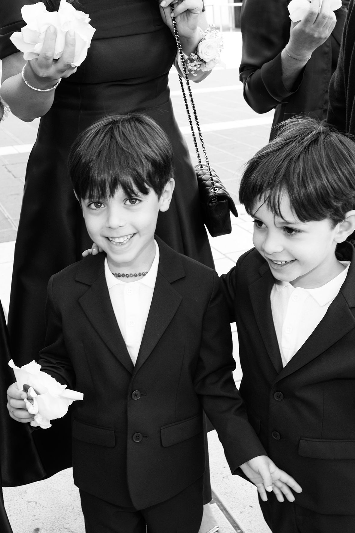 Two young boys in matching black suits share a joyful moment at a formal event.