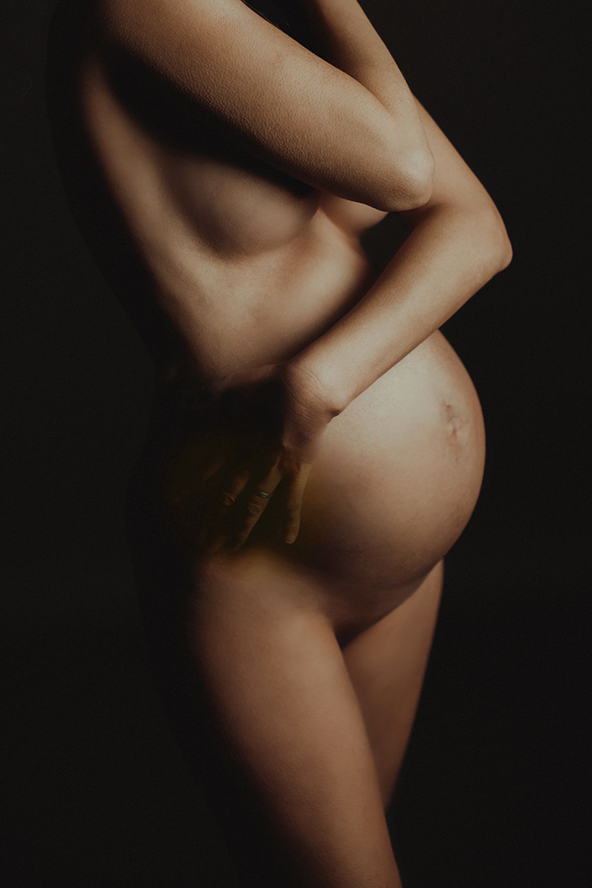 Artistic black and white maternity photo showing silhouette of pregnant belly against dark background.