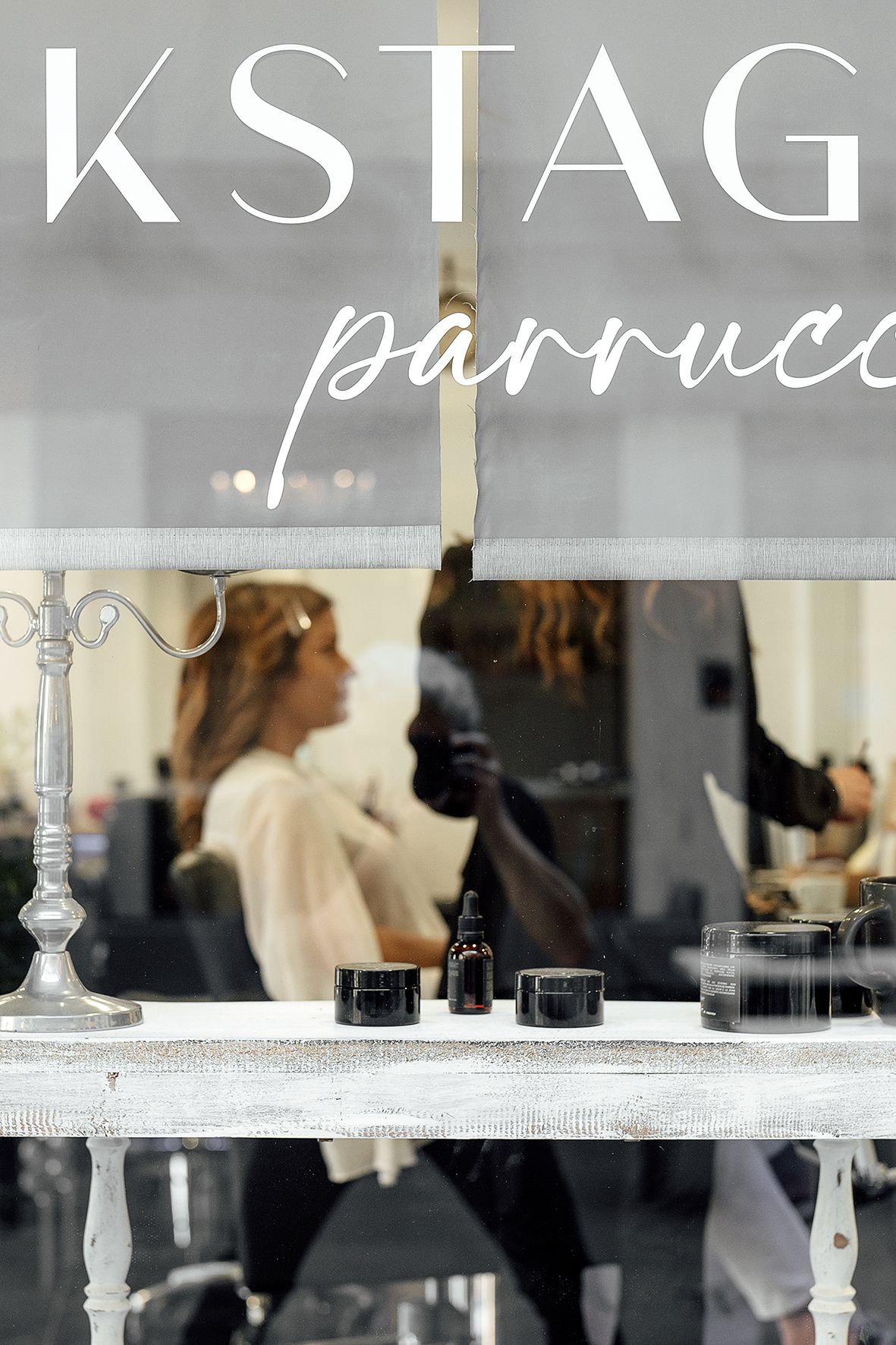 A storefront window displays 'KSTAG Parrucce' signage with elegant decor and salon styling stations visible inside.