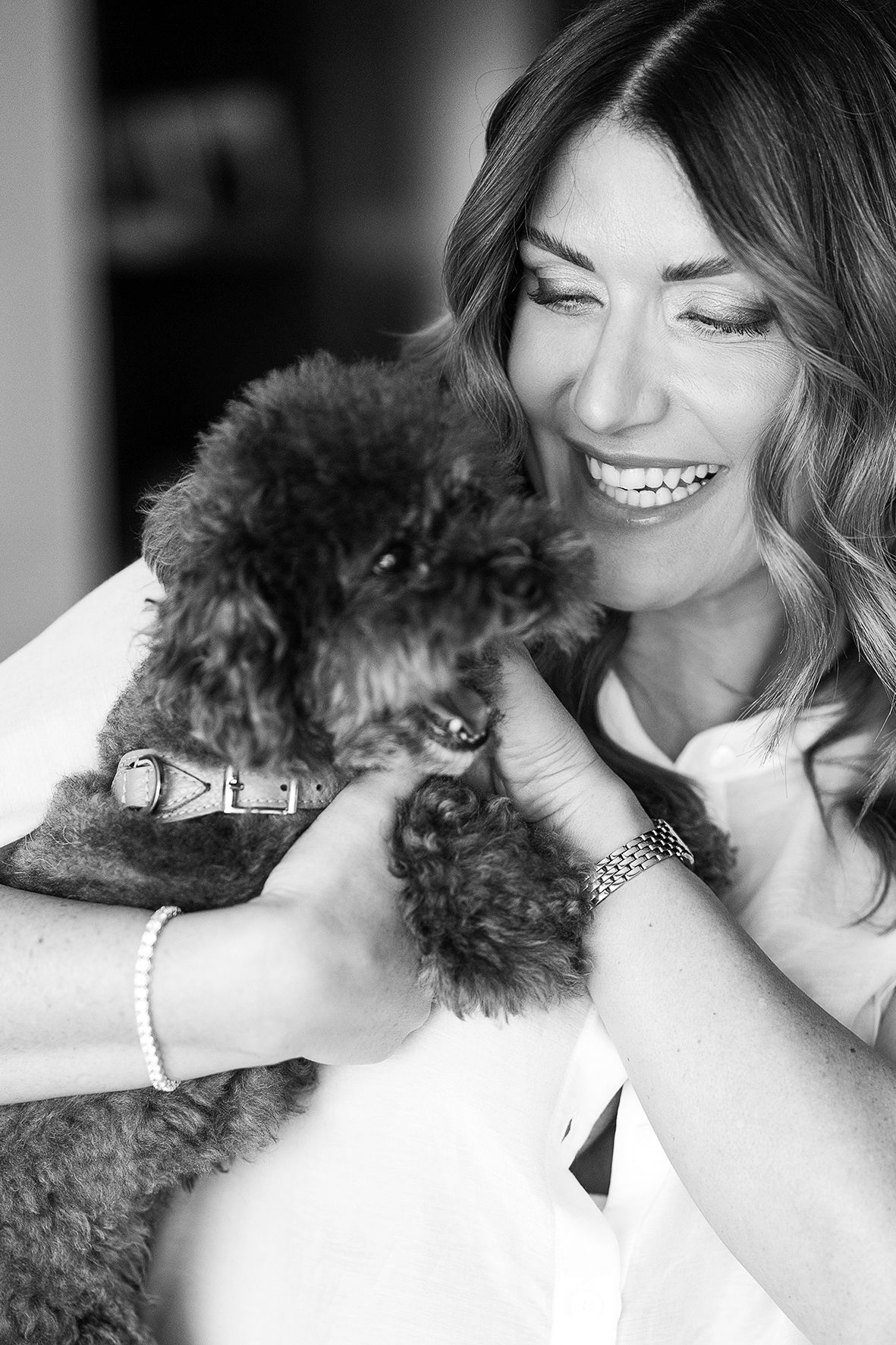 Black and white portrait of someone holding and smiling at a happy fluffy black poodle wearing a collar.