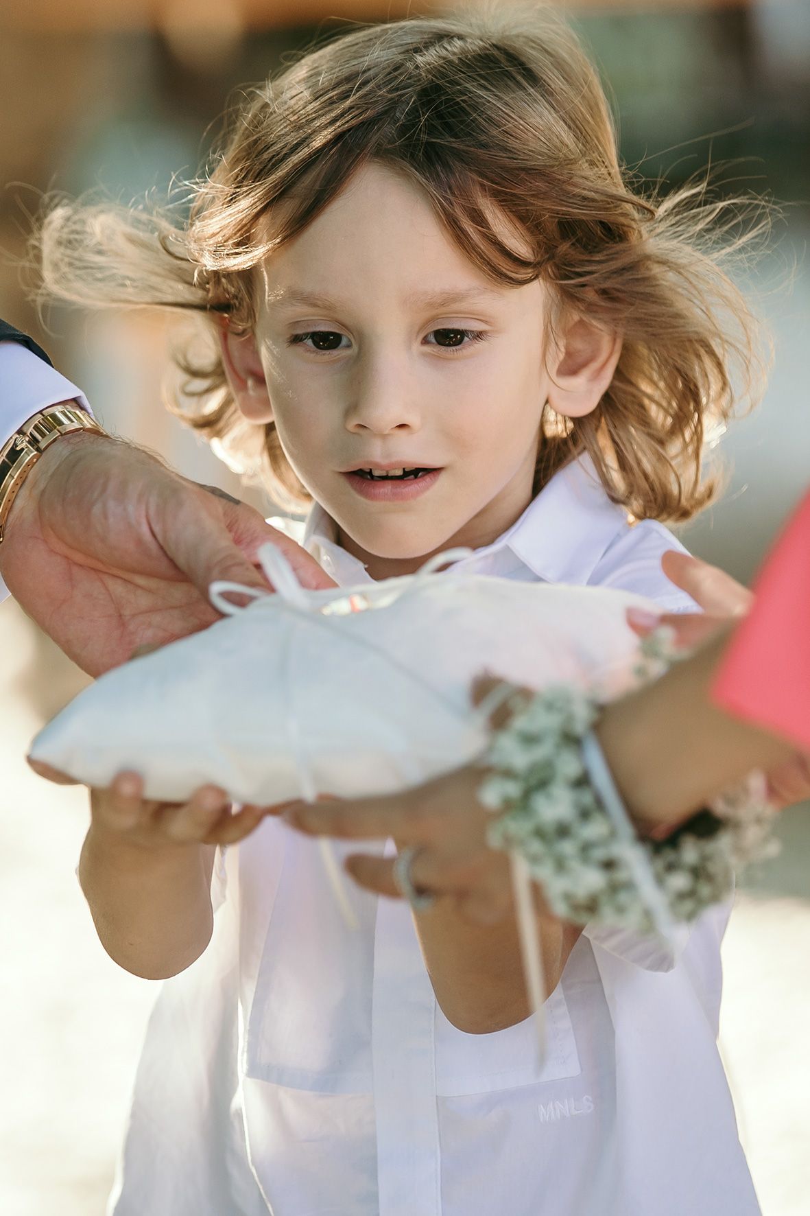 Child in white dress holds up and examines a pair of dance or ballet shoes in glowing sunlight.