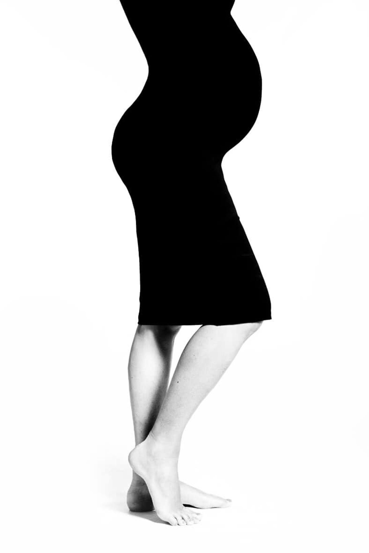 High contrast black and white silhouette of a pregnant woman in a fitted dress standing in profile view.