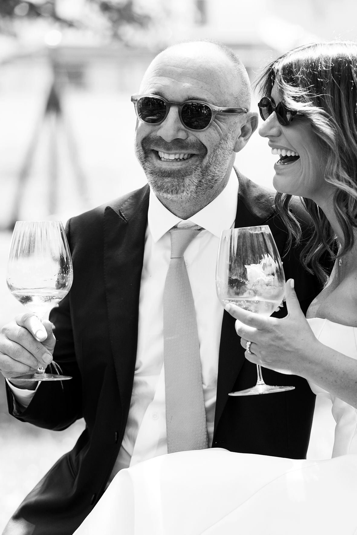 Black and white photo of two people joyfully sharing wine glasses at an elegant celebration.