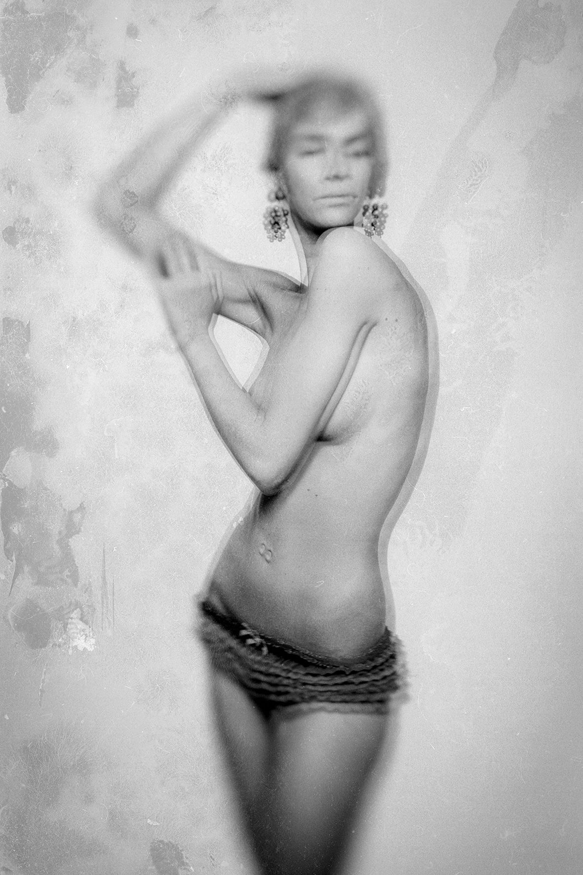 Artistic black and white fashion photograph showing a sensual pose against a textured background.