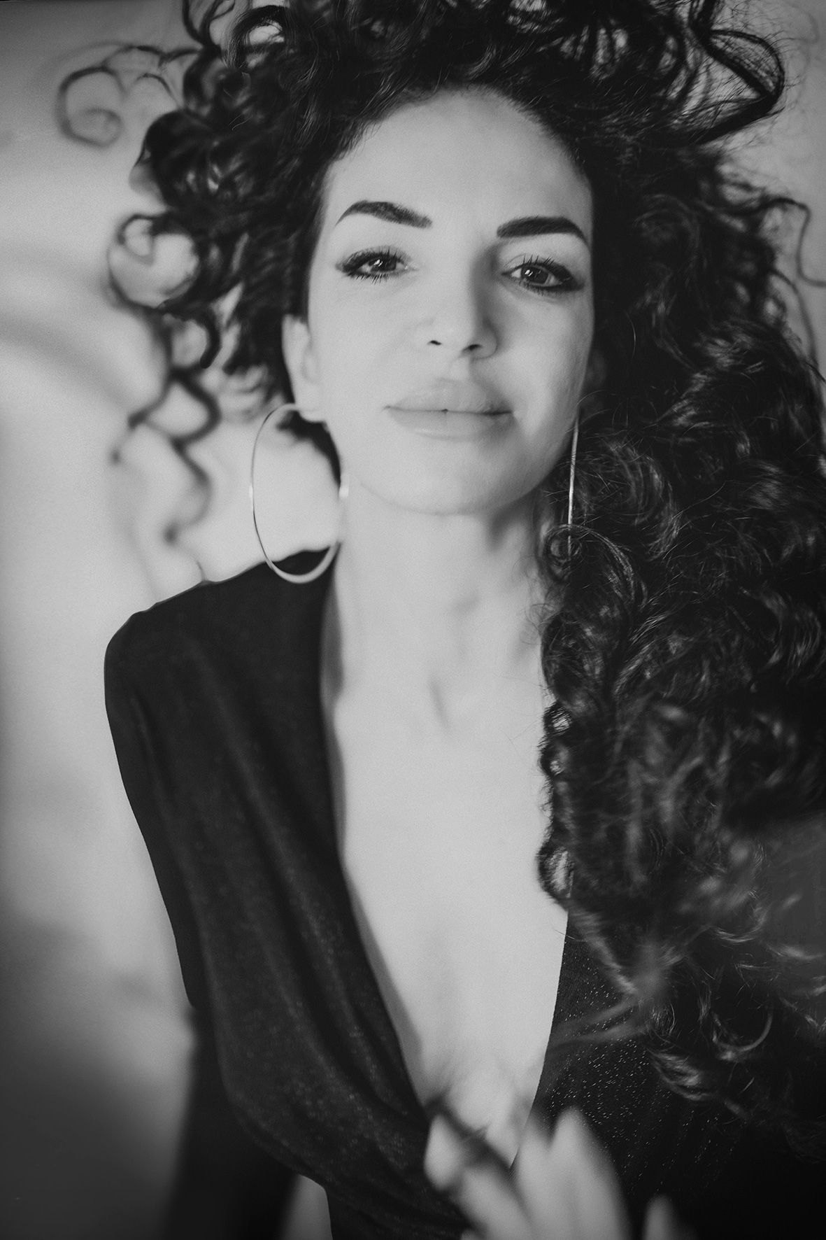 Black and white portrait featuring dramatic curly hair and hoop earrings in an intimate close-up shot.