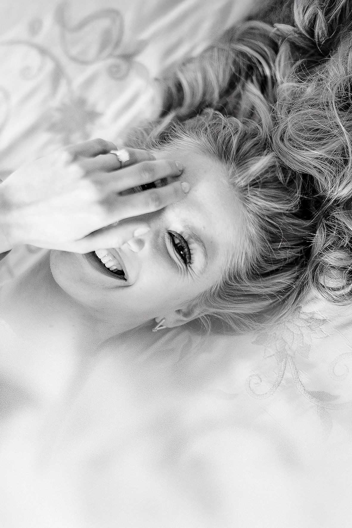 Black and white lifestyle portrait shot laying on bed with messy hair and joyful laughter.