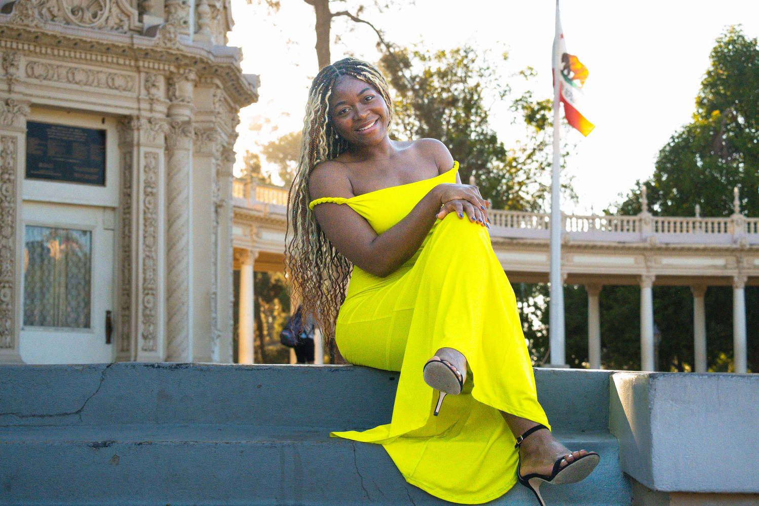 Person wearing a bright yellow off-shoulder dress poses in front of ornate architecture.