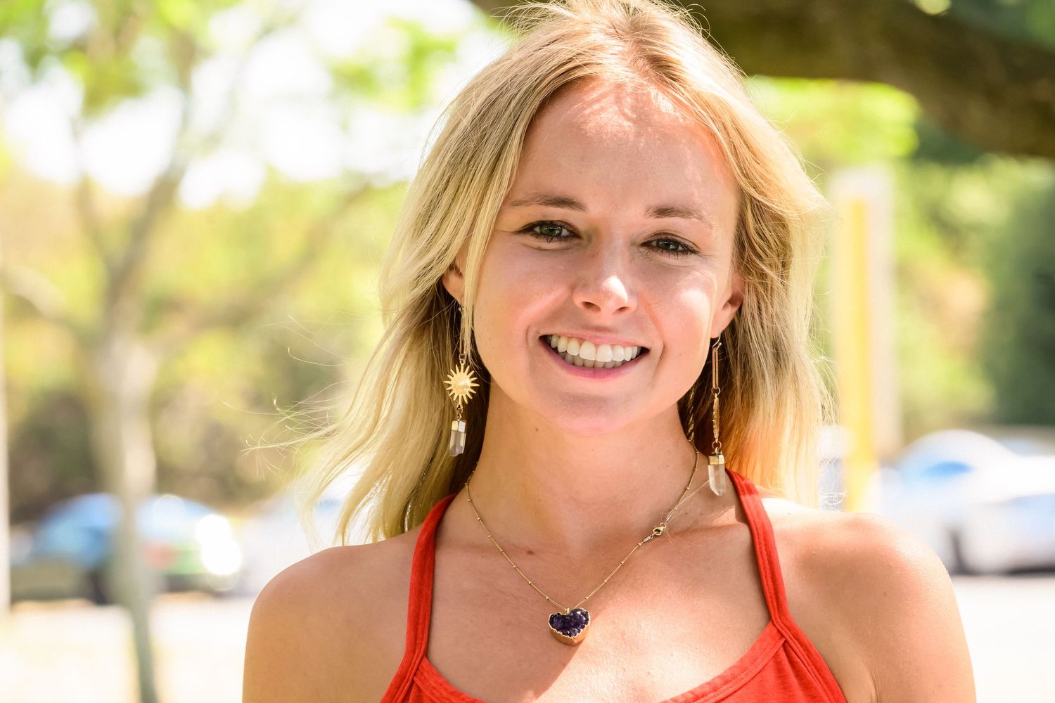 Portrait of someone in a red top smiling brightly on a sunny day.
