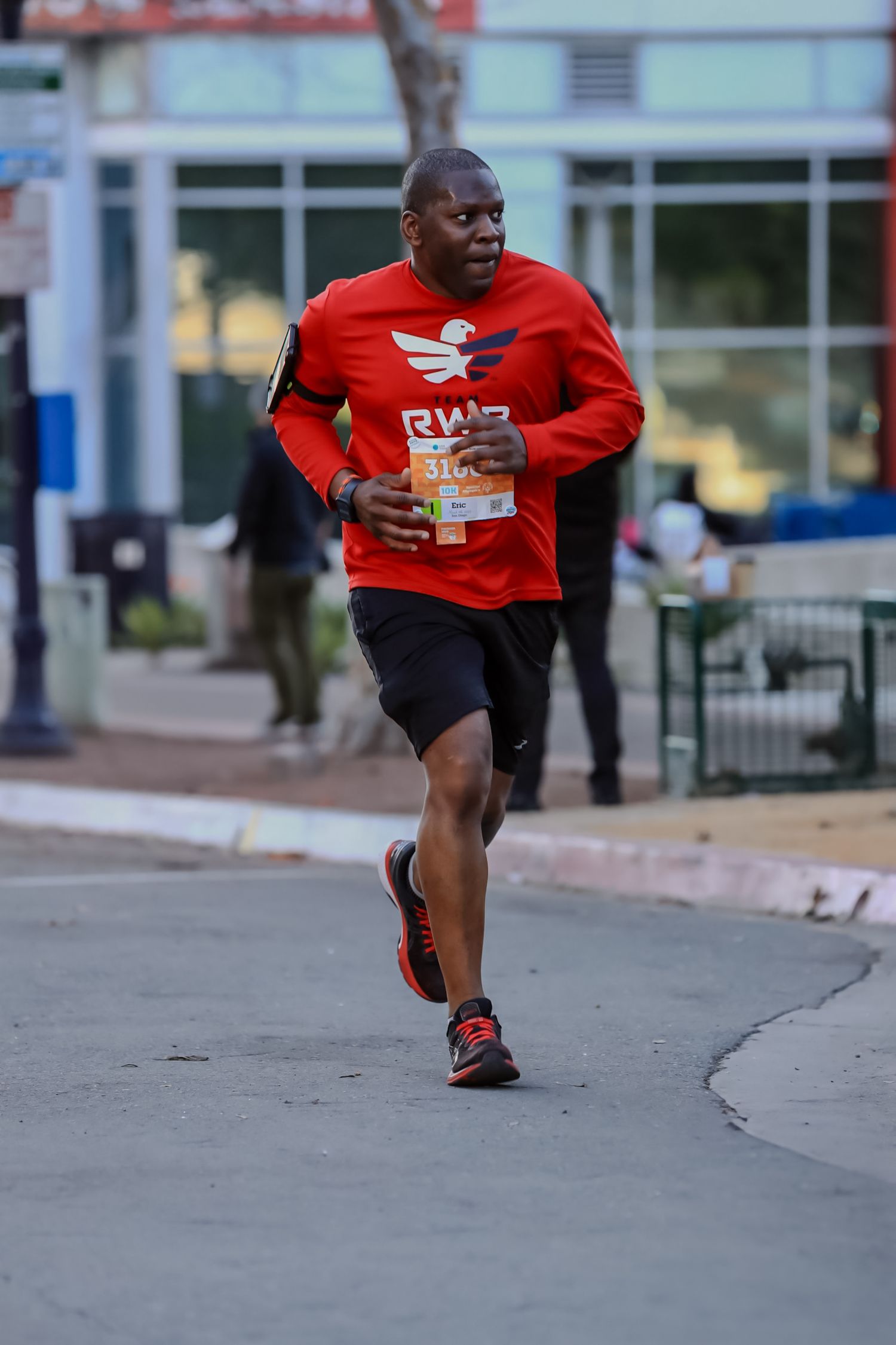 Runner in red sportswear moving along an urban sidewalk during training.