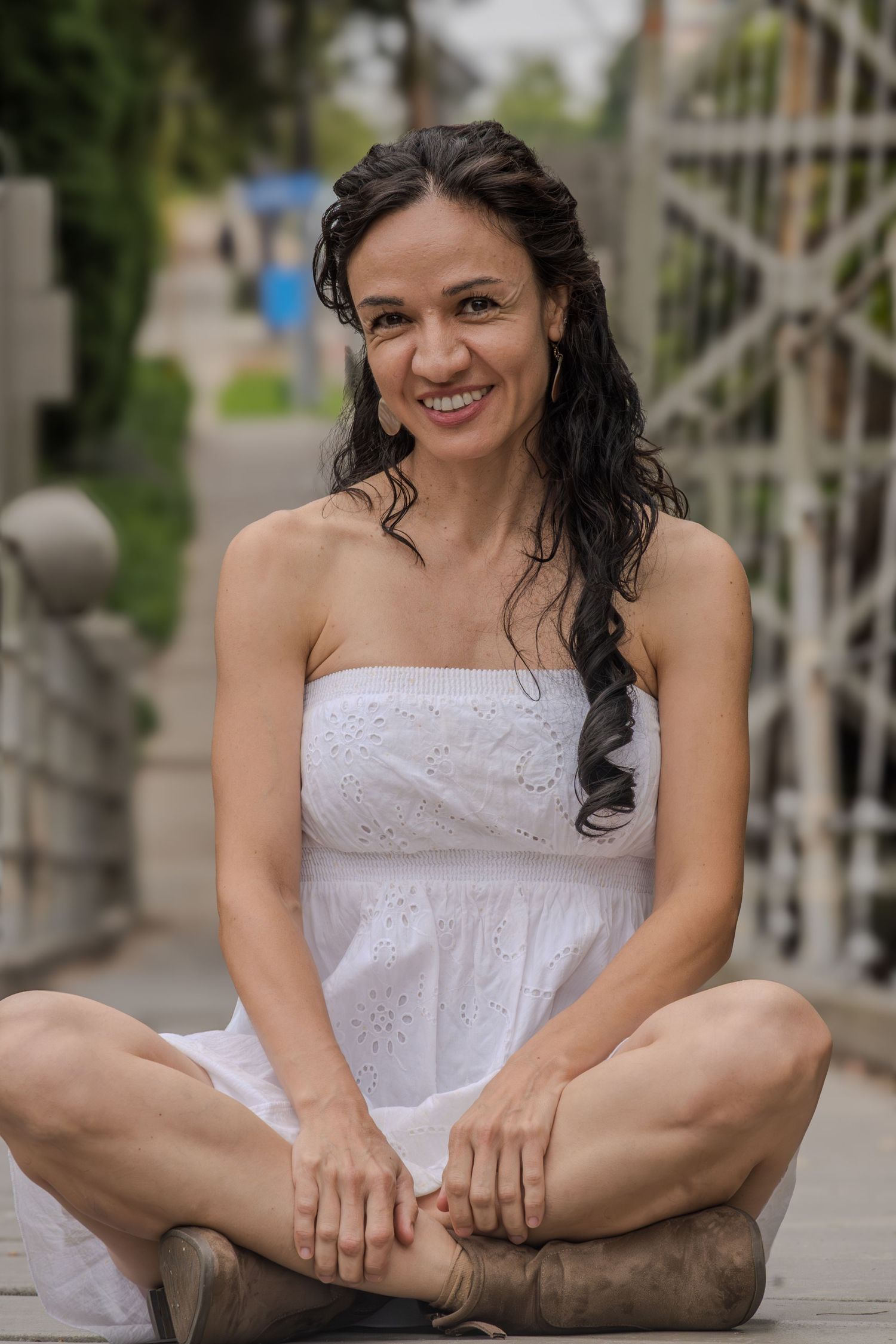 A person in a white dress sits on the ground demonstrating yoga flexibility poses in an outdoor setting.