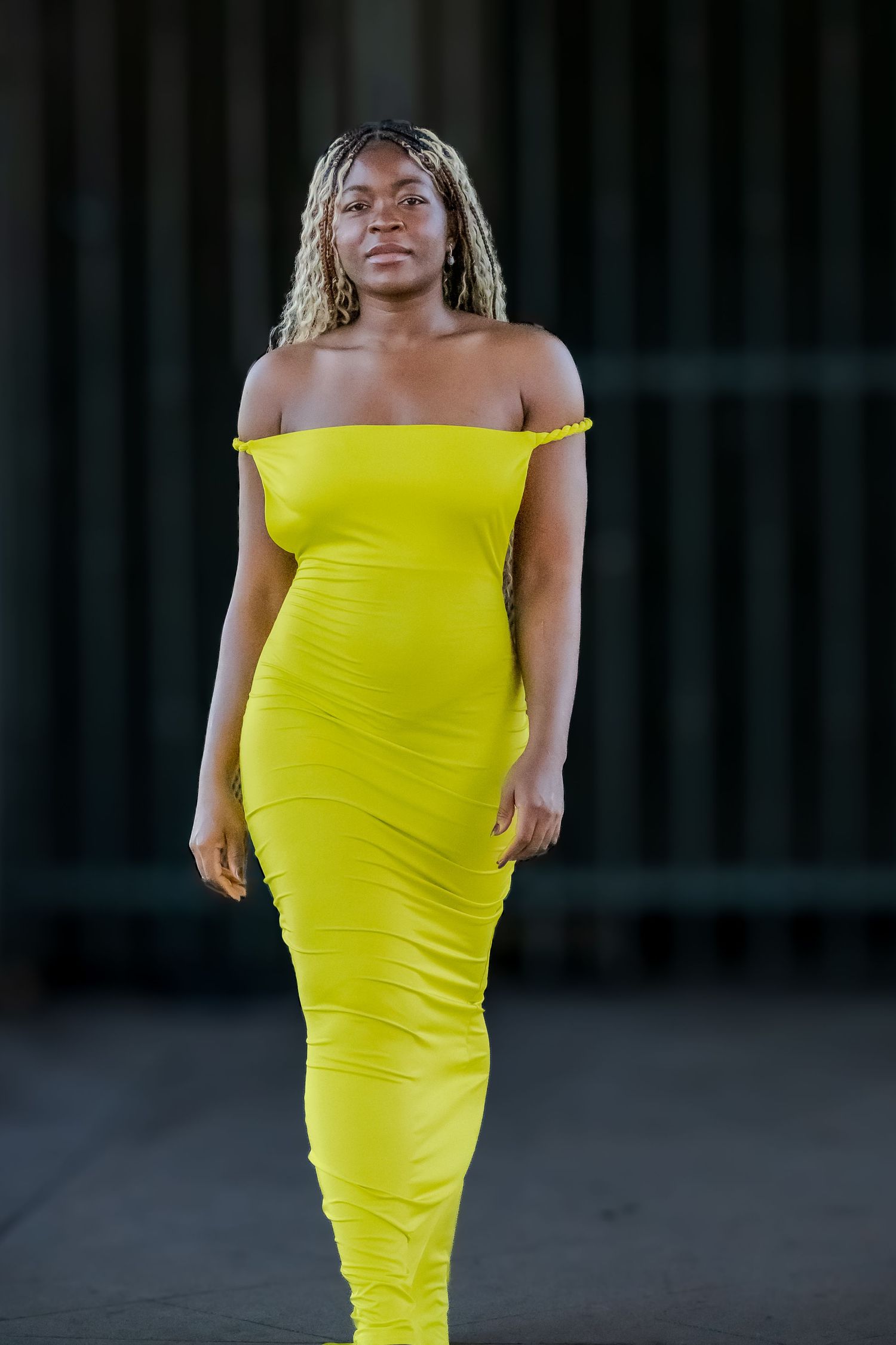 Figure in a vibrant yellow form-fitting dress photographed against a dark background.