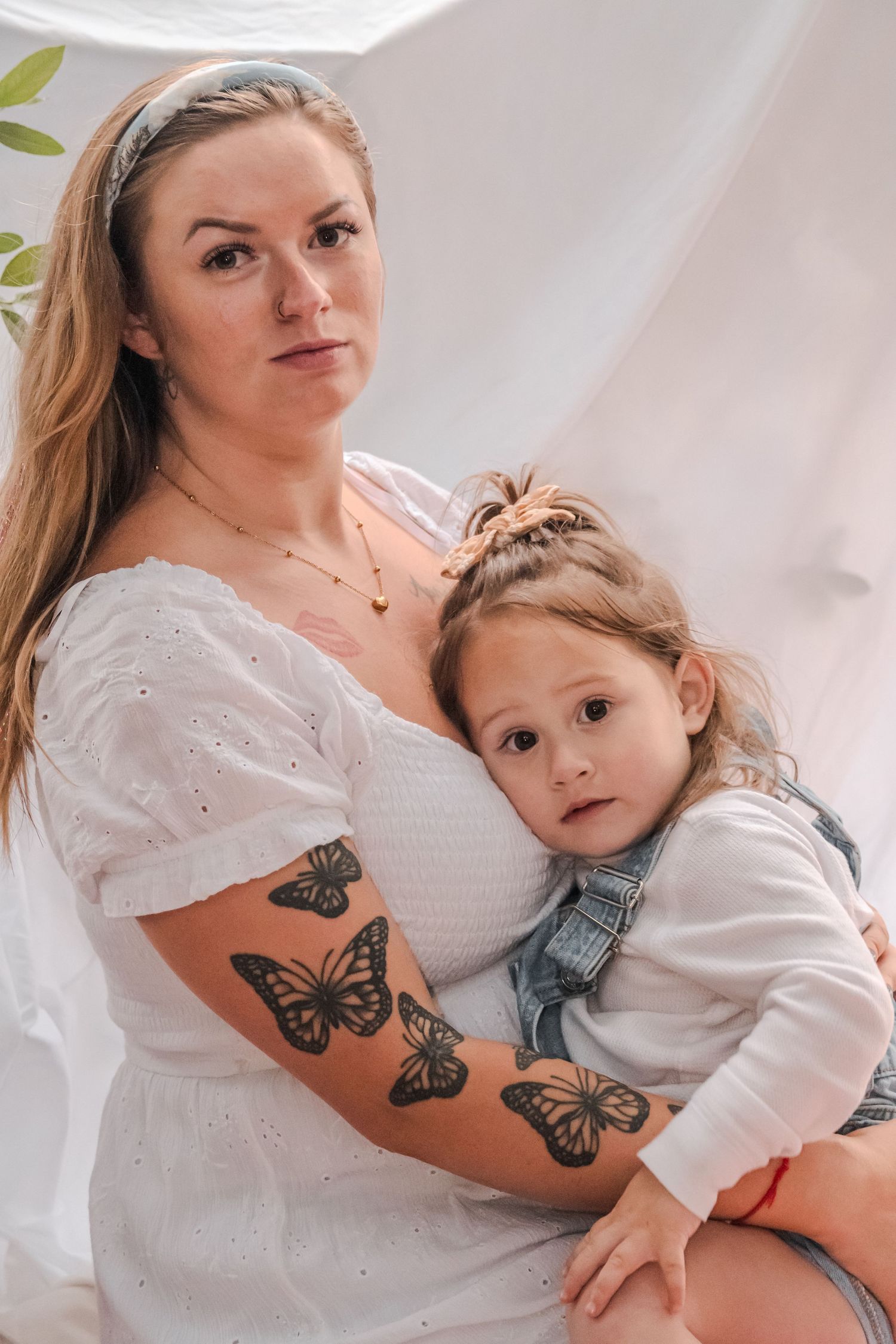 Intimate portrait showcasing butterfly tattoos and tender maternal moments against white backdrop.