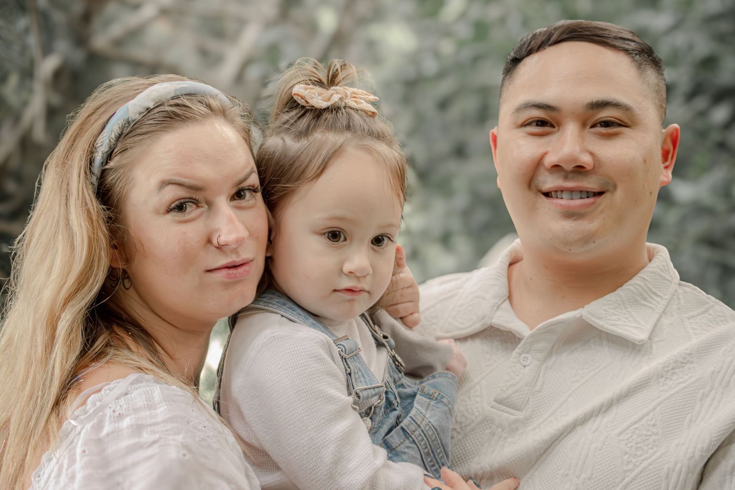 Family wearing coordinated neutral outfits embraces during outdoor photo session in natural setting.