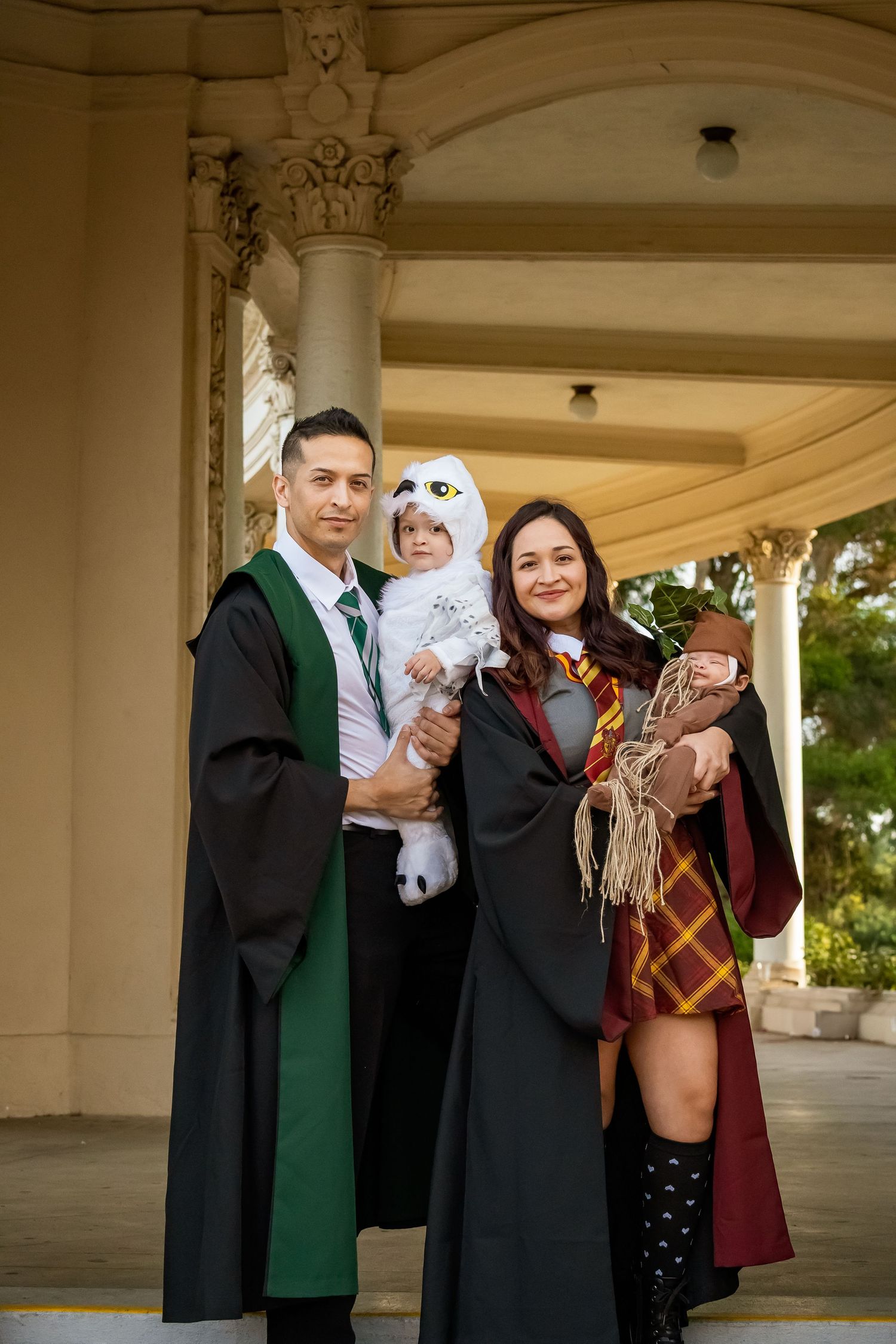 Family photo with parents in Hogwarts graduation robes posing with children in magical creature costumes.
