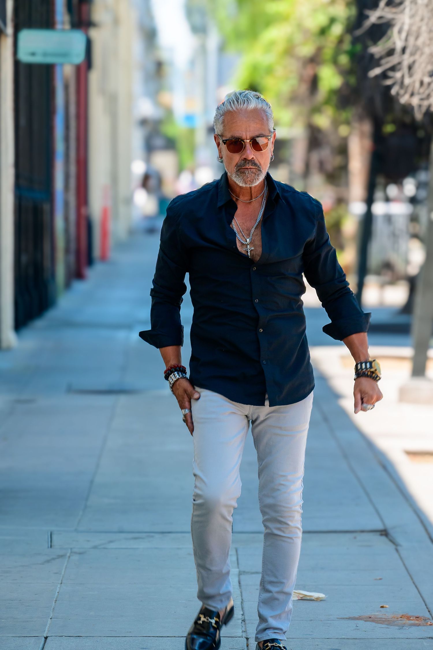 Person in navy shirt and white pants walking confidently down a city sidewalk.