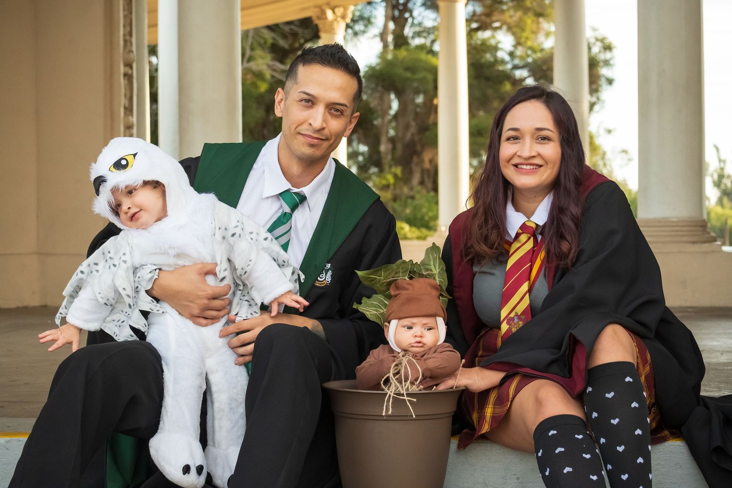 Family photo with parents in Hogwarts graduation robes posing with children in magical creature costumes.