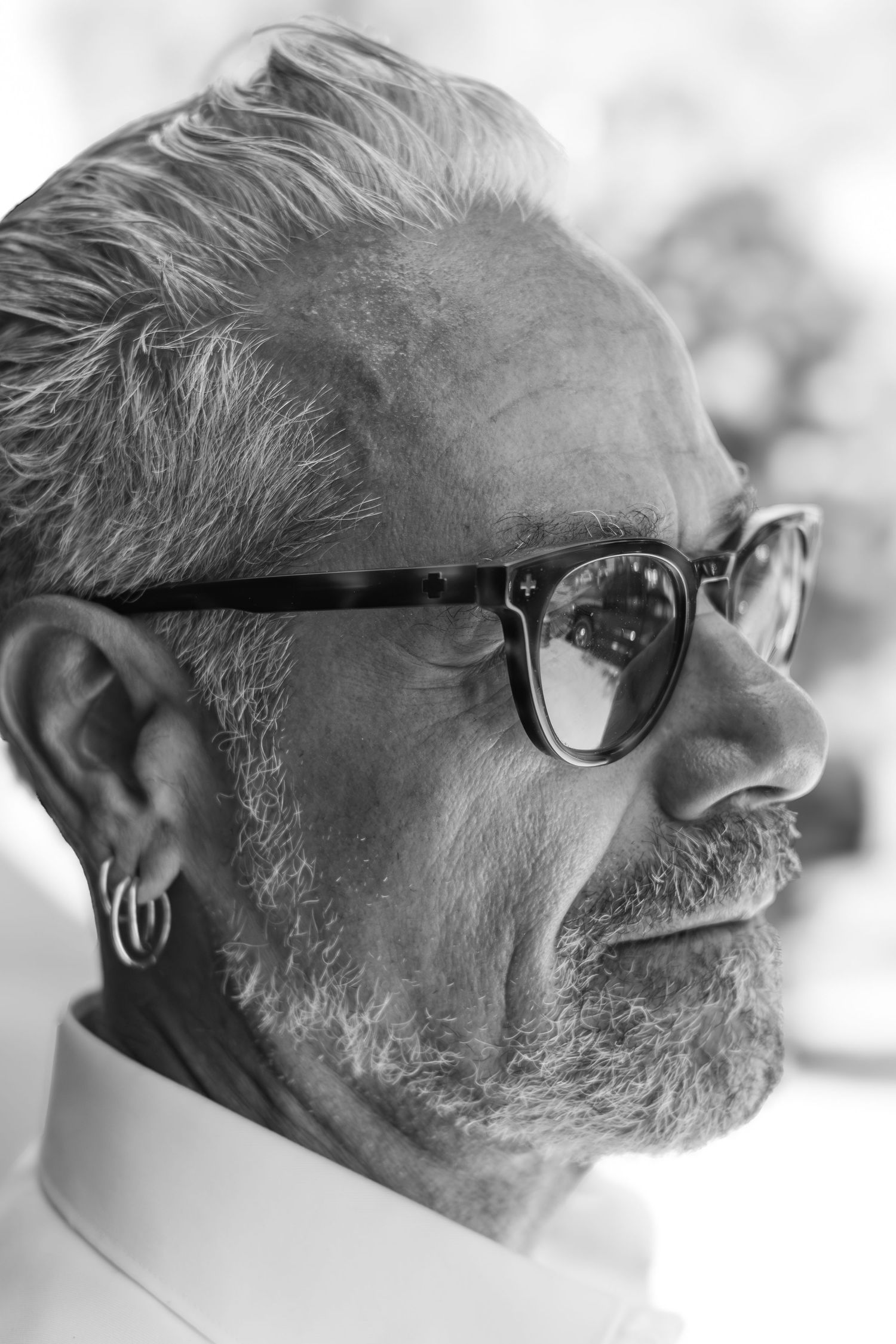 A black and white profile portrait of someone wearing dark-framed glasses and a white collar with silver hair and beard.