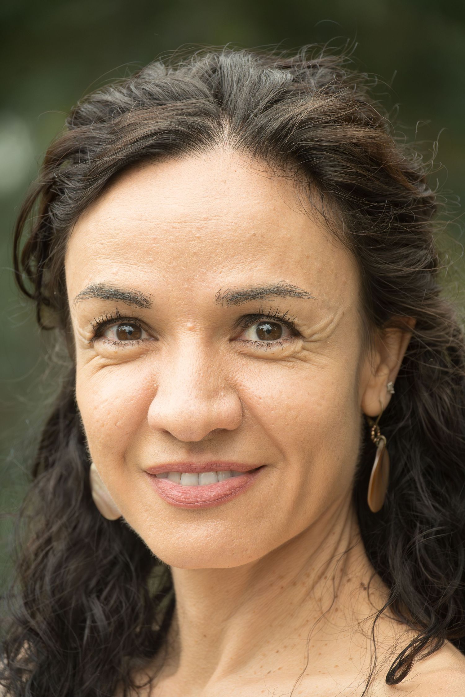 Close-up portrait of someone with dark curly hair and a warm smile against a blurred green background.