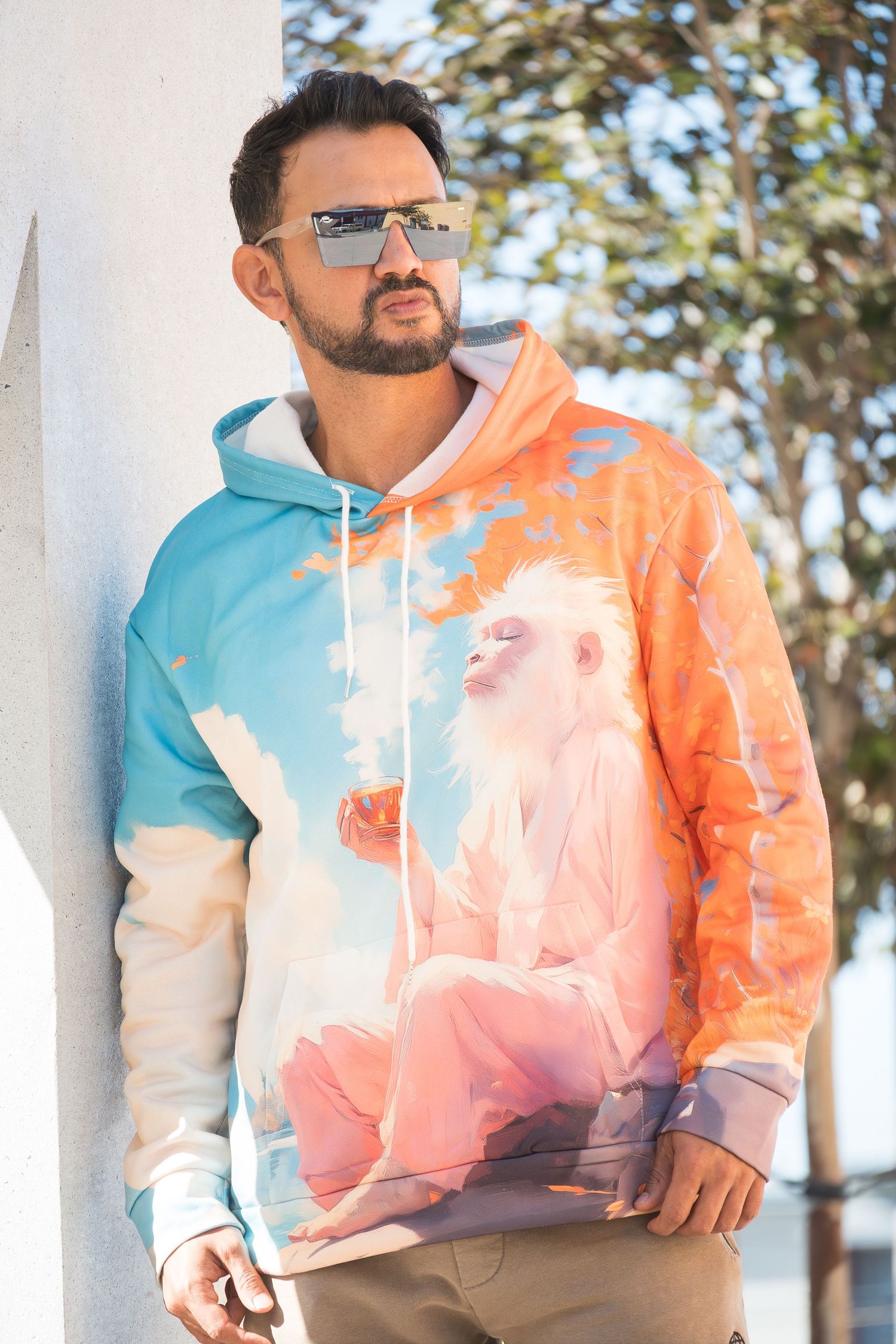 Person wearing stylish tie-dye hoodie in orange, blue and white poses outdoors against natural backdrop.