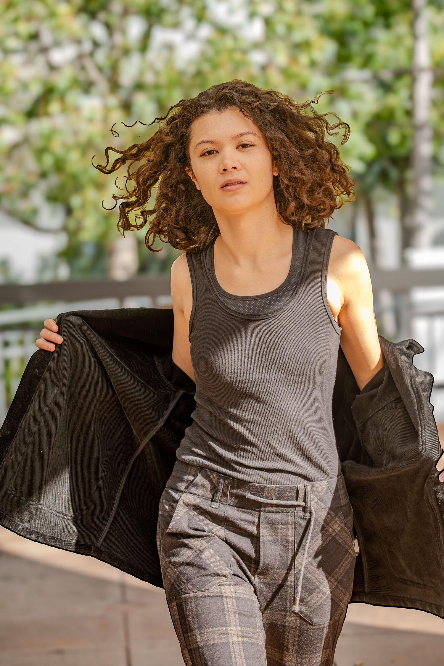 A dynamic fashion sequence shows a model in a gray tank top and plaid pants removing a black jacket in an outdoor setting.